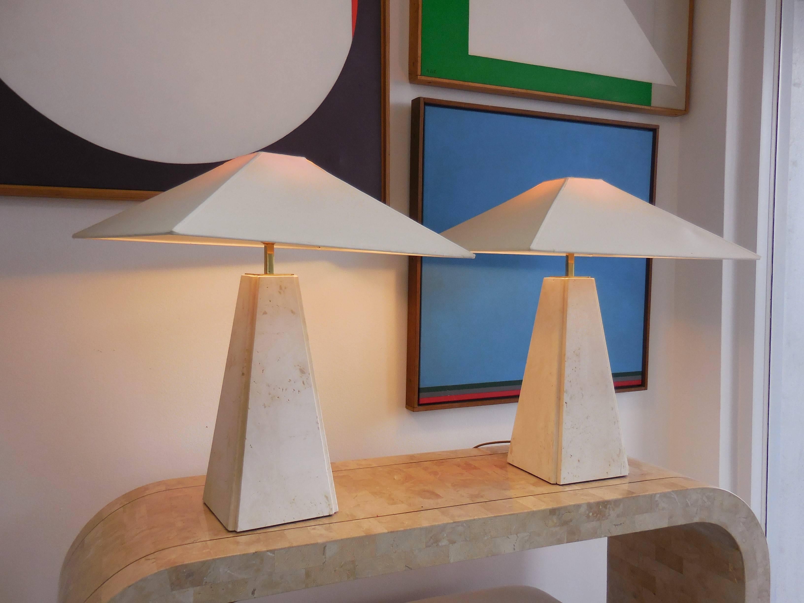 A pair of Italian travertine lamps. Stylizes obelisk shape with the original linen shades. Brass hardware. Marble base is 16