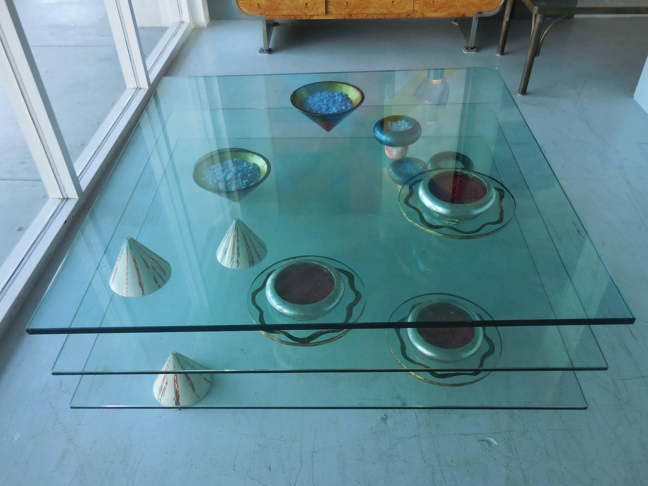 This is a tri-level coffee table by Artist Carmen Spera. Multiple movable sculptural pieces are actually balancing on an axis and holding the glass surfaces in place. The look is magical, surprising and so unique. Some of the elements are wood with