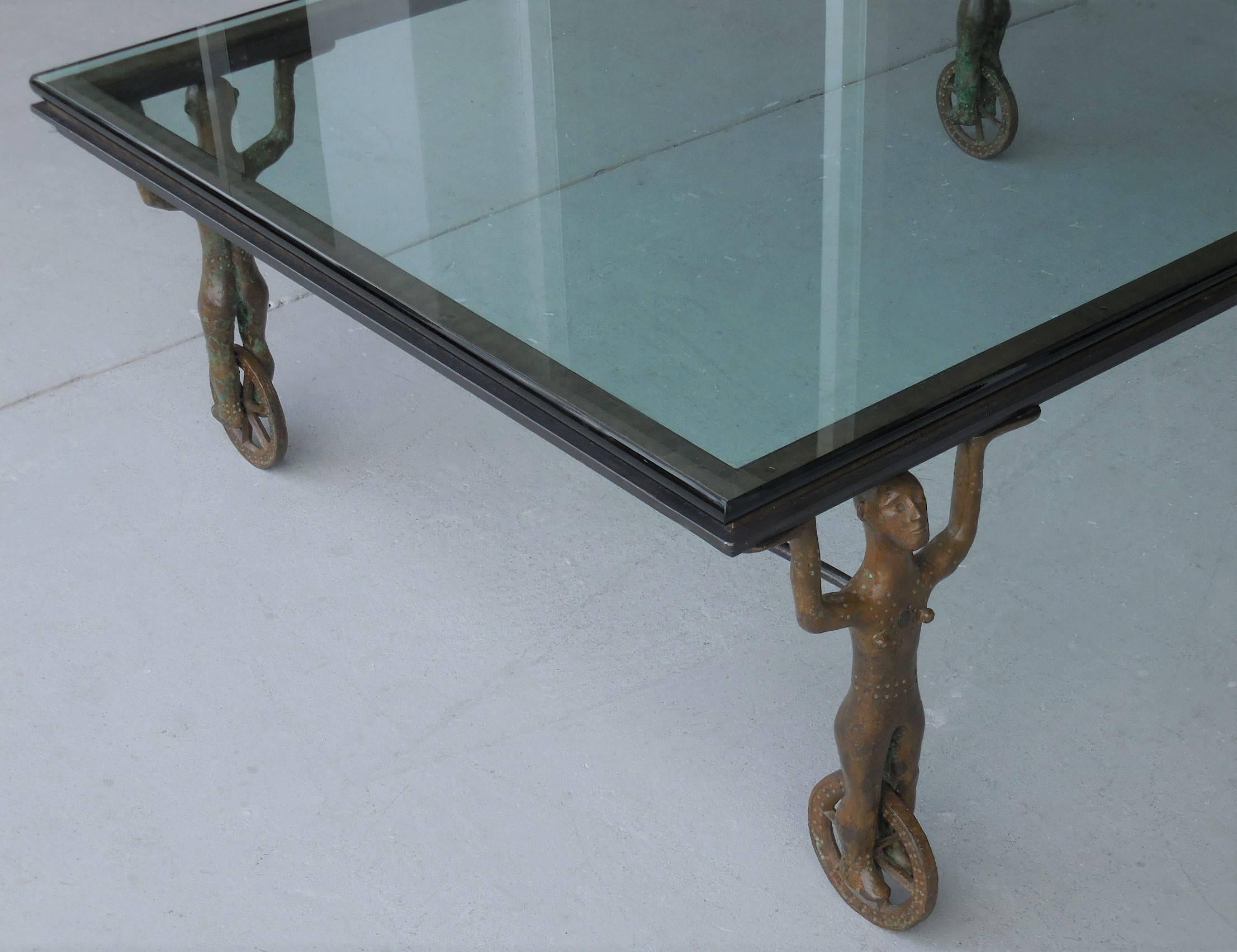 Most interesting coffee table. Bronze figures on wheels. Signed, numbered and dated on underside of frame. The four bronze caryatid elements have a unique flair to them, reminiscent of work by the Giacometti brothers.  Glass top is 3/4