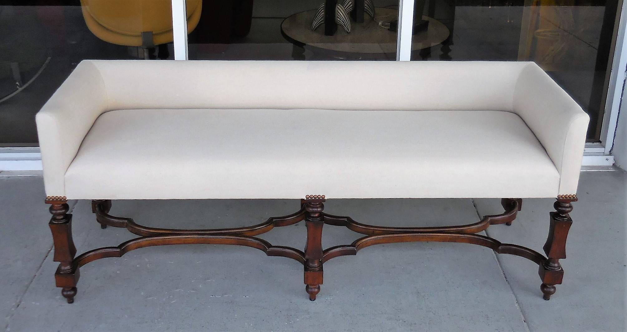 A long bench or settee by Baker. Wood frame and linen upholstered seat. Very versatile, could be standing by itself or at the foot of the bed. Would work with a queen or king-size bed.