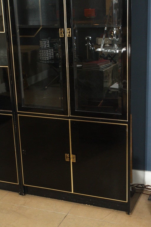 Black lacquer case piece with brass hardware and trim detail. Glass double doors on each end.