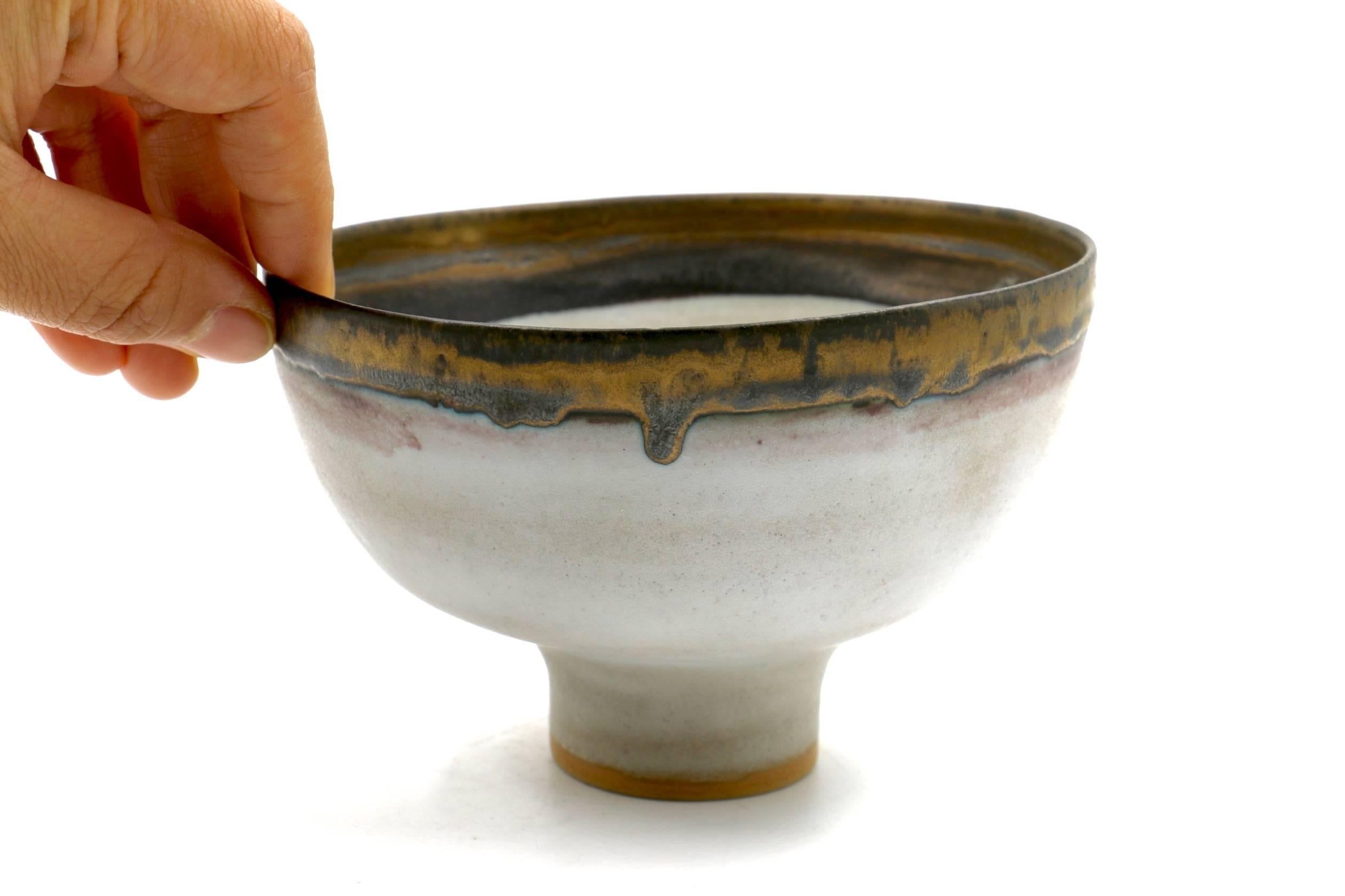 Tall-footed bowl with Artist initials at the bottom of the bowl. Rare, beautiful example of Lucie Rie's delicate pottery. White glaze with bronze slip rim with mauve details under the rim. Measures 5 3/8 x 5 1/4 x 3 3/8 inches. Signed by the artist.