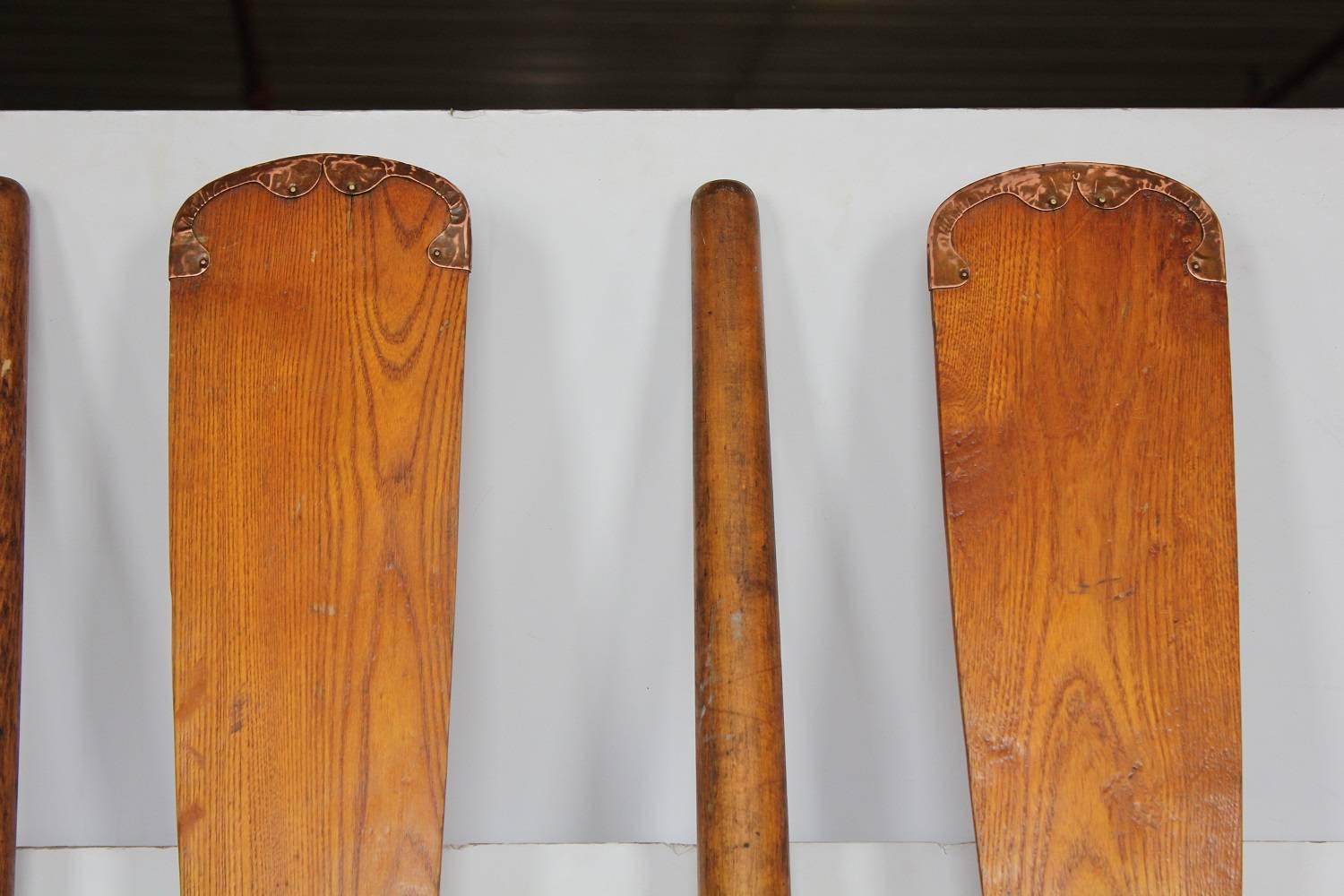 Collection of four vintage wood oars with leather handles and metal ends.