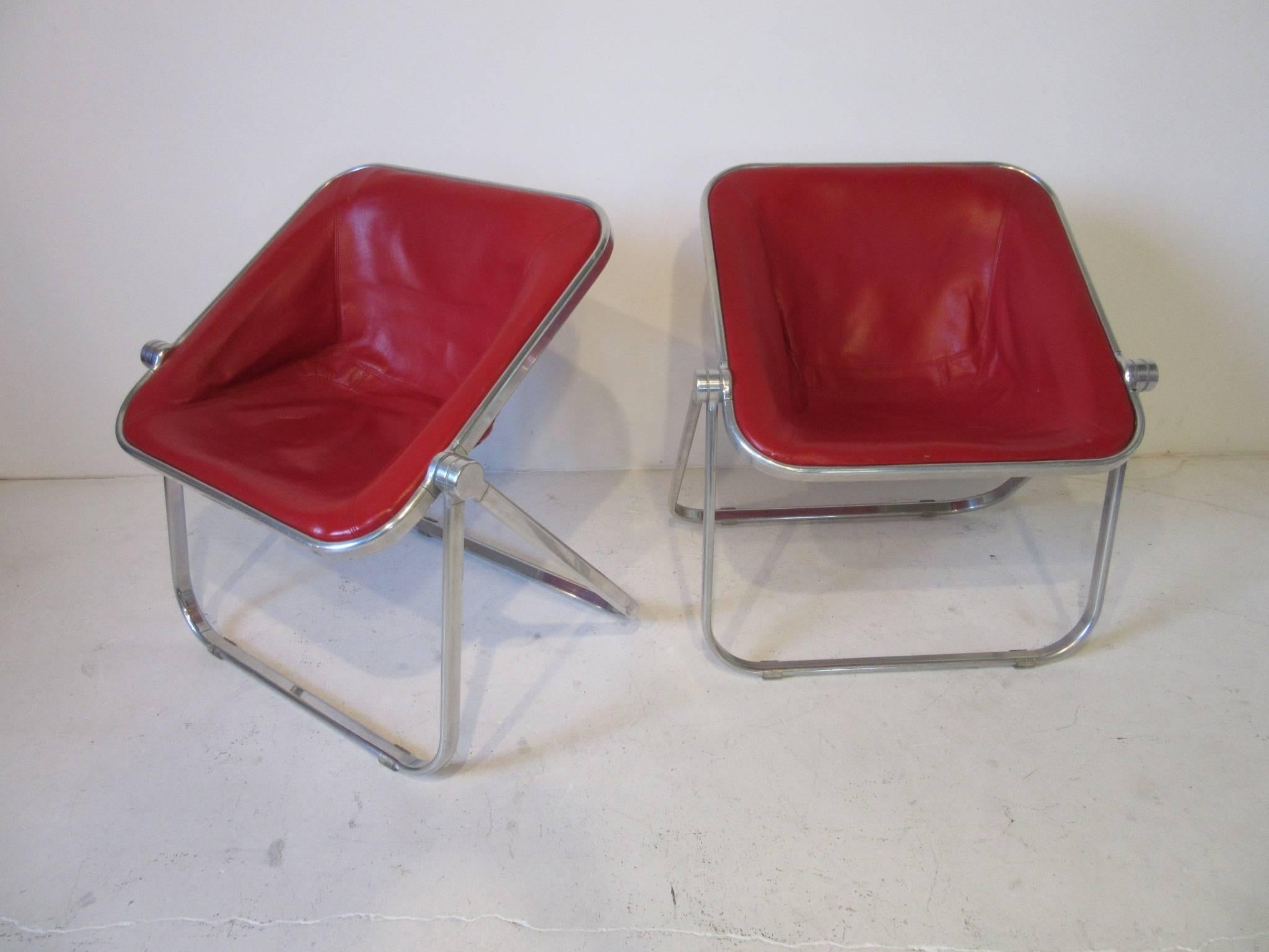 A pair of aluminum framed and lip stick red leather Plona chairs, these well designed chairs are comfortable and fold flat for storage which is great for a smaller space. Retains the manufactured label Plona Made in Italy JSC Divisione Sedie.