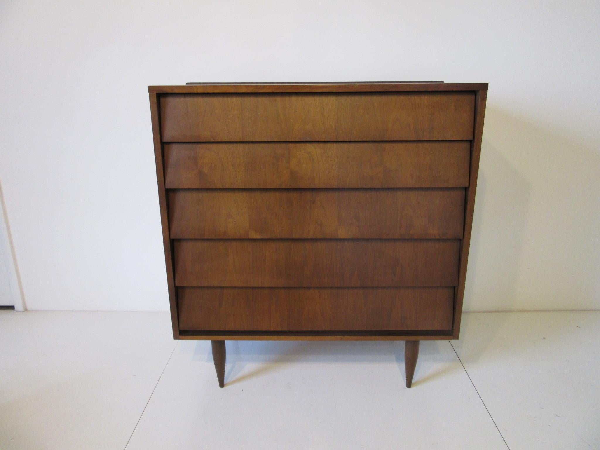 A tall dark walnut dresser chest with five slanted drawer fronts, raised lipped edge to
the back of the top all sitting on conical legs. A great Mid Century look in the manner of Florence Knoll.
