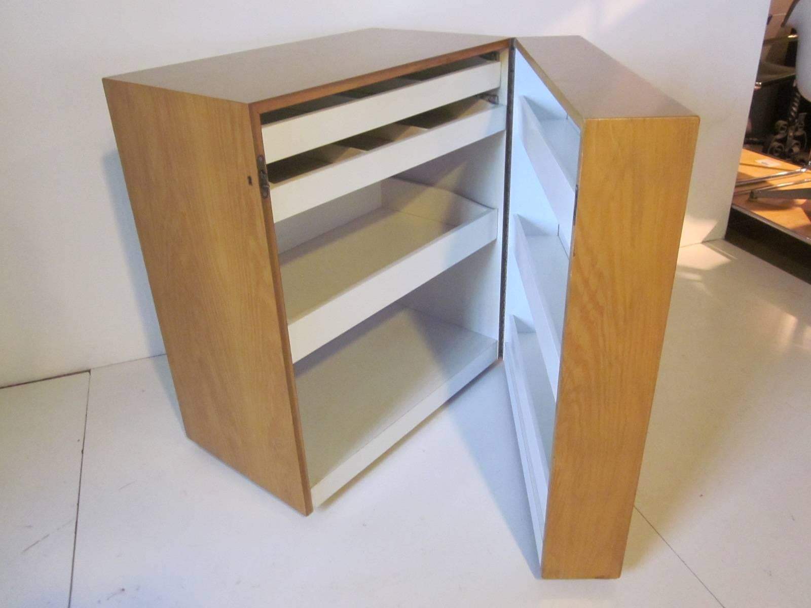 A unique sever or bar in the shape of a cube with the front door on a wheel for easy opening, inside there's three pull-out shelves with compartments a lower storage area and three shelves on the door. Housed in a flamed wood grain cabinet finished