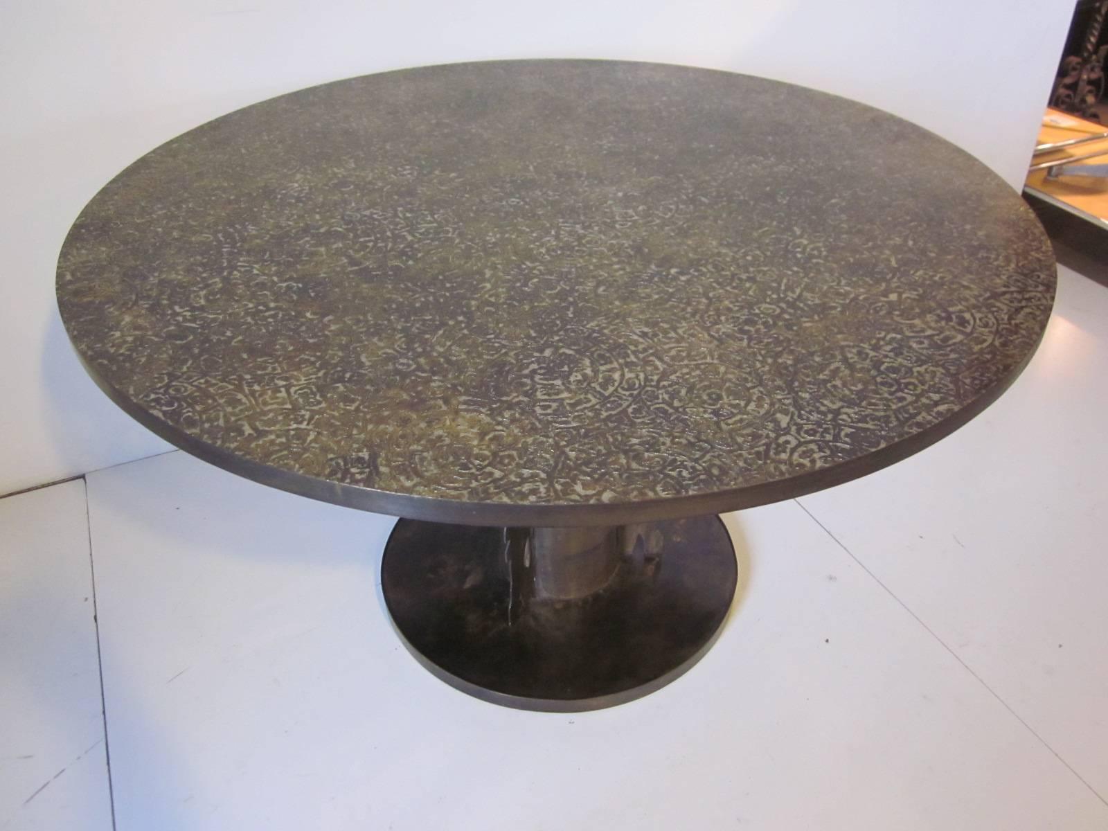 A beautiful handcrafted dining or game table with acid etched relief designs to the top in bronze with a pewter wash bringing out the details. Sitting on a organic styled column support and round base with the engraved signature of the artist /