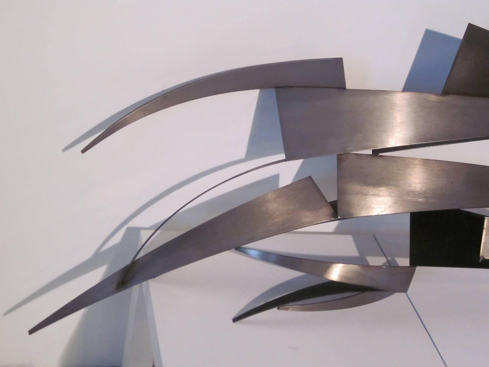 A stainless steel and satin black metal wall sculpture with welded and cut pieces that flair out to each side, hanger mounts are attached to the reverse manufactured by Curtis Jere.