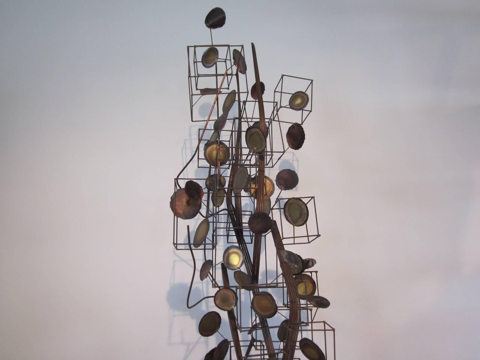 A large abstract tree styled sculpture with a inner trunk of metal rods surrounded by welded open boxes and torched cut and burned round leaf or medallions. A detailed and well put together piece of art with steel base which it sits on and can by