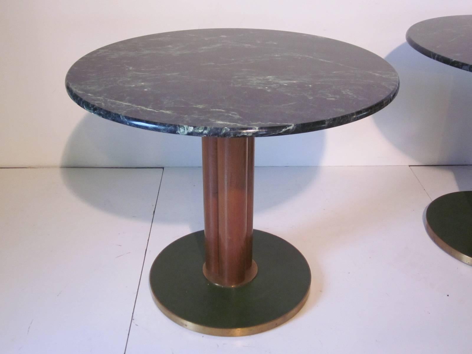 Striking green marble game or dining tables sitting on mahogany tri columned pedestals with green leather and brass trimmed bases. An elegant design from the master of taking the characteristics of the designs from the past and simplifying them into