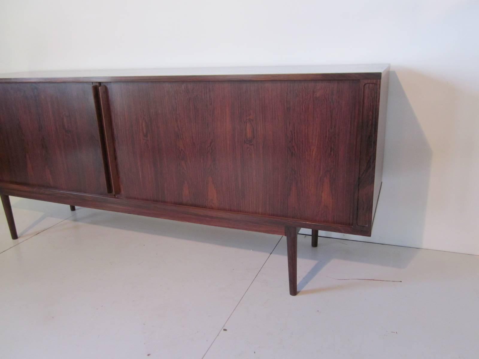 A rich and dark Brazilian rosewood tambor door credenza with five center internal pull-out drawers and storage on each side with a total of three adjustable shelves. Retains the manufactures label to the finished back side, Løvig made in Demark.