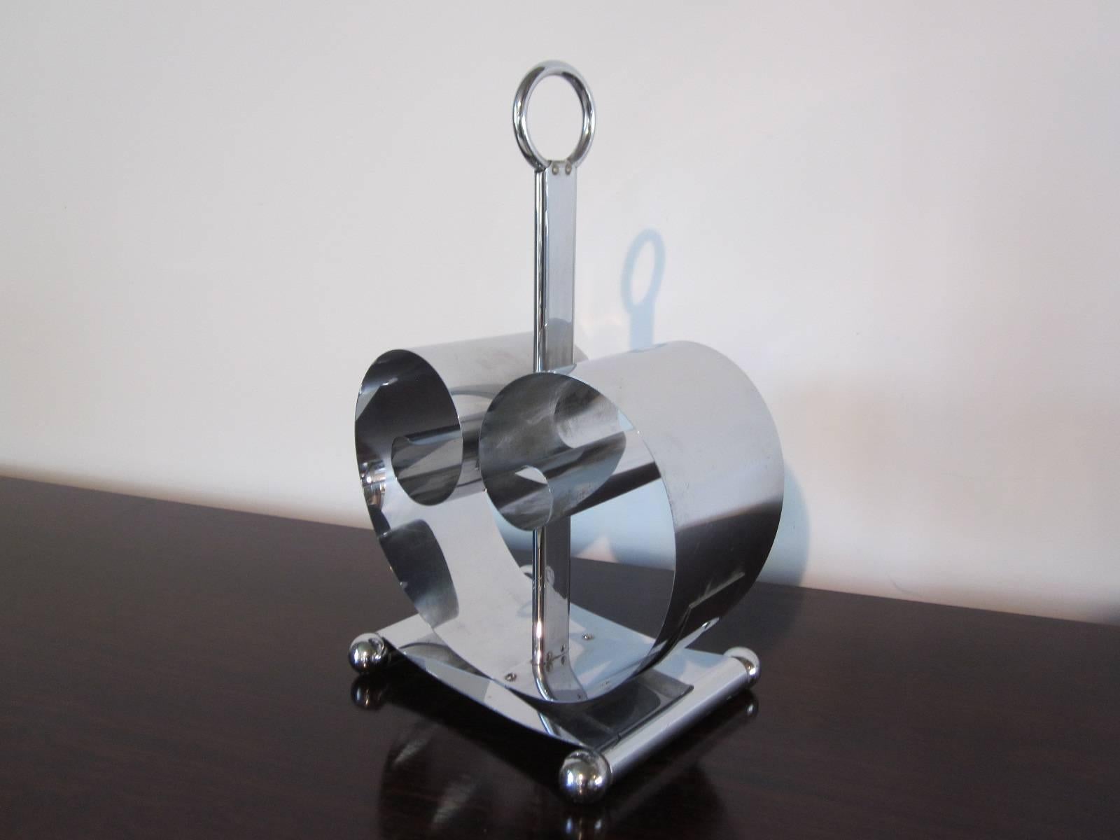 A chrome-plated stainless steel magazine rack with tension spring holder, metal loop handle sitting on a ball footed platform, manufactures imprint to the bottom, Revere, Rome, NY.