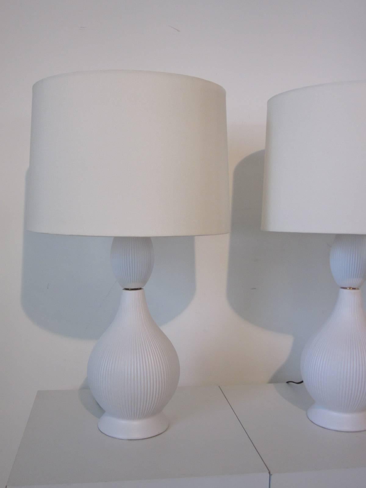 Ceramic white matte finished pottery table lamps with ribbed design, brass details and linen shades and brass final.