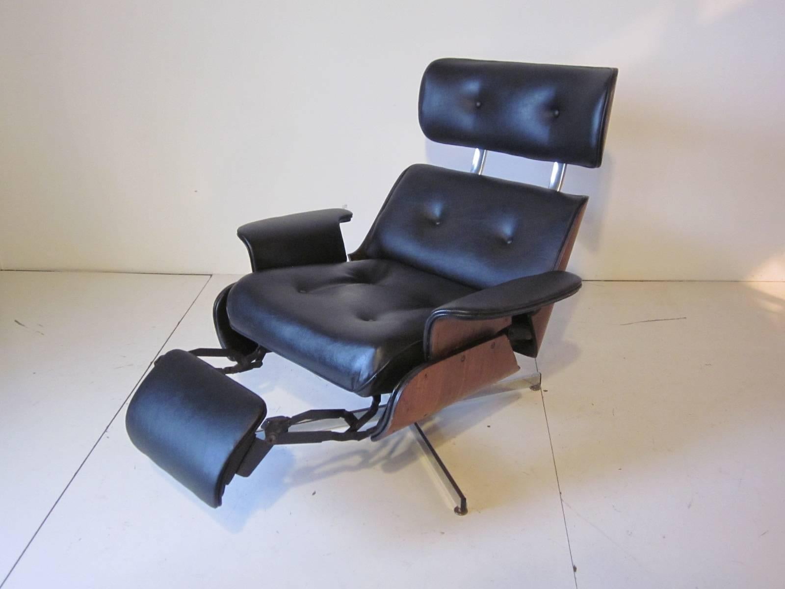 A Ply Craft bent walnut plywood lounge chair in black leatherette with a built in foot rest in the style of lazy boy, chrome X base and large flared arms. The chair swivels and extends in three modes, lounge chair, tilting back with foot rest