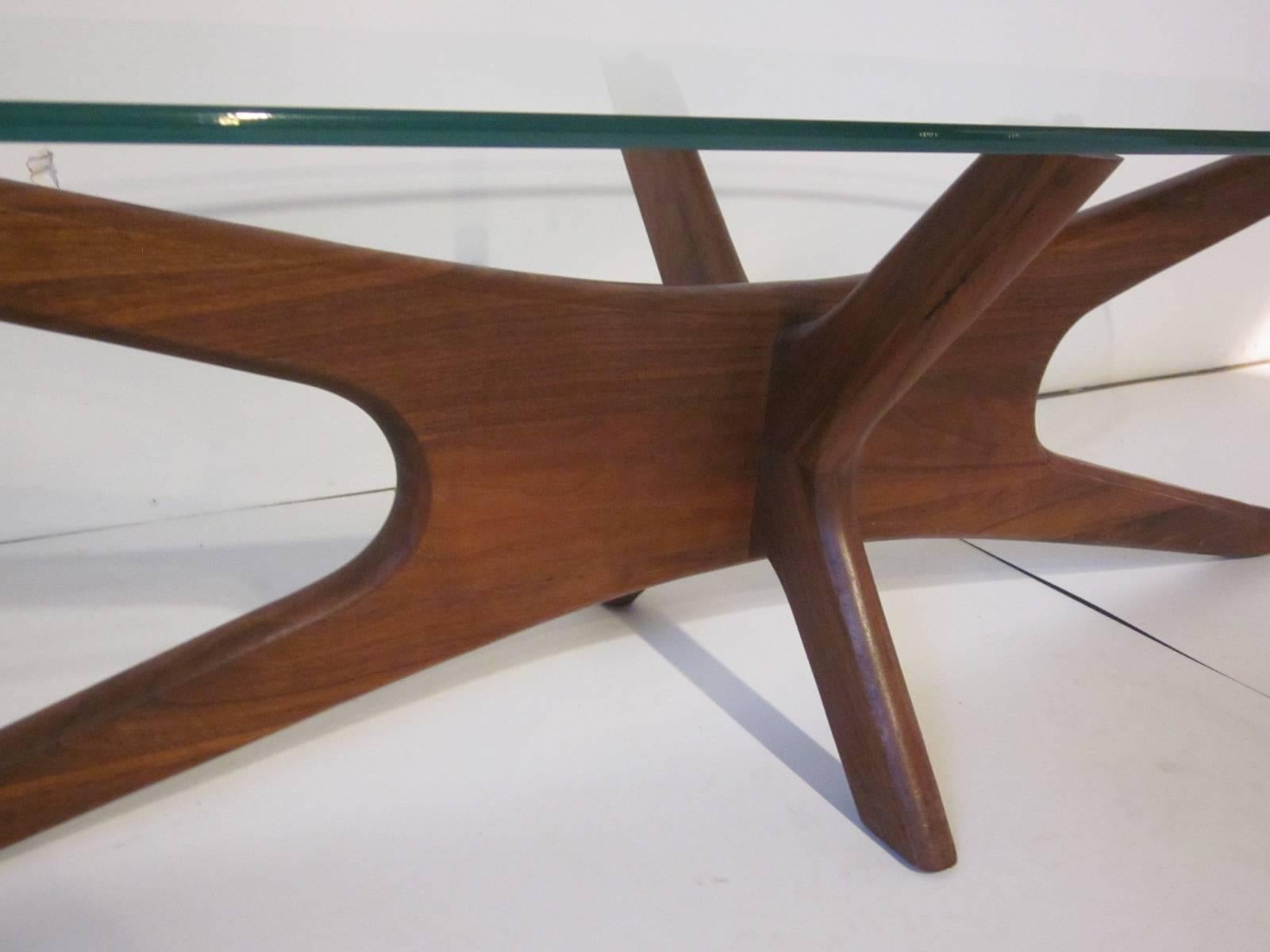 A Jacks coffee table with sculptural solid walnut base and oval styled glass top manufactured by Craft Associates.