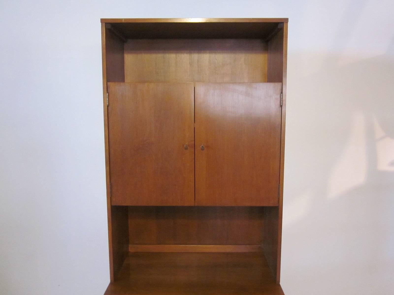 A solid maple two-piece Paul McCobb cabinet with upper and lower adjustable shelves behind the double doors, brass golf tee pulls for the hardware, a lot of storage for a smaller space. From the Planner Group manufactured by the Winchendon Furniture
