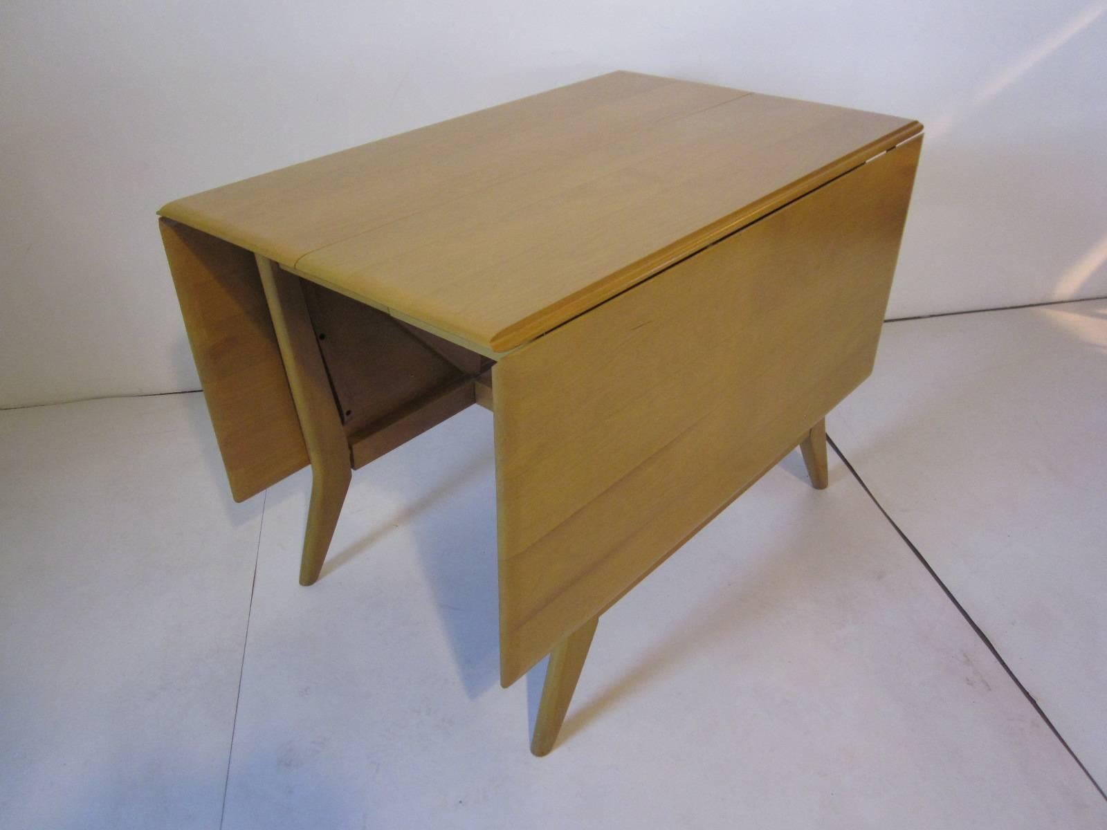 A drop-leaf Harmonic extension dining room table in a wheat tone with butterfly supports to the table ends, includes two 10