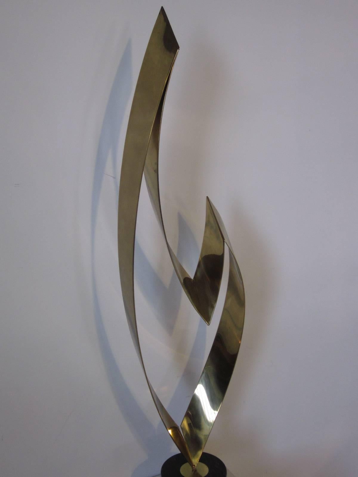 A large thick brass flame sculpture mounted on a grayish marble base, the piece can be rotated to any viewing angle, faint signature to the brass 