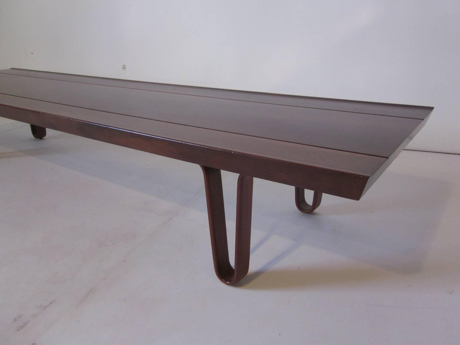 A well grained medium mahogany Long John coffee table or bench with sculptural bentwood legs and grooved detail lines to the top. Retains the early green metal manufactures label, Dunbar Furniture Company Bern Indiana.