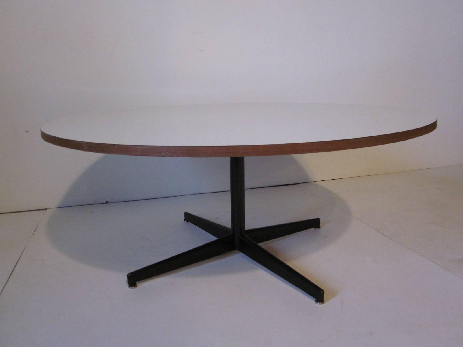 A round coffee table in the style of Herman Miller and George Nelson with white laminate top, wood trimmed border, satin black star metal base and domes of silence foot pads.