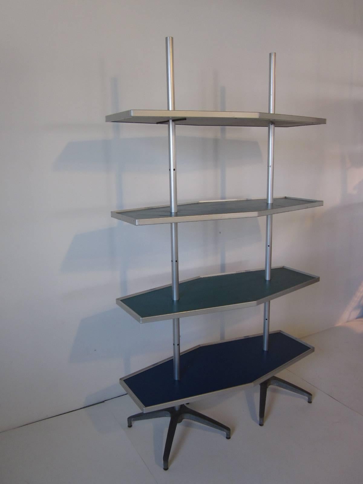 A Mid-Century modern industrial shelving unit used for displays with four mod shaped adjustable shelves, two in turquoise and two in dark blue with aluminum trim. Matching aluminum poles with shelve pins slip into the star bases and all this breaks
