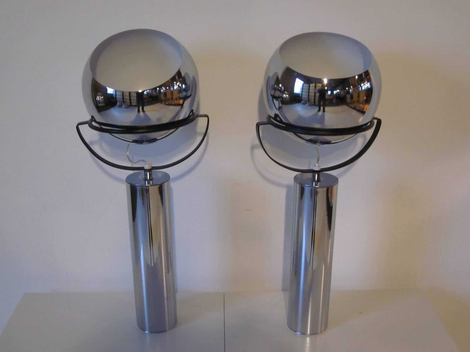 A pair of chrome adjustable shade table lamps with the ball cradled by a sculptural metal upper bracket with tube base. The light switch is at the bottom of the ball and the ball has a adjustment for up or a slight angle, manufactured by the Robert
