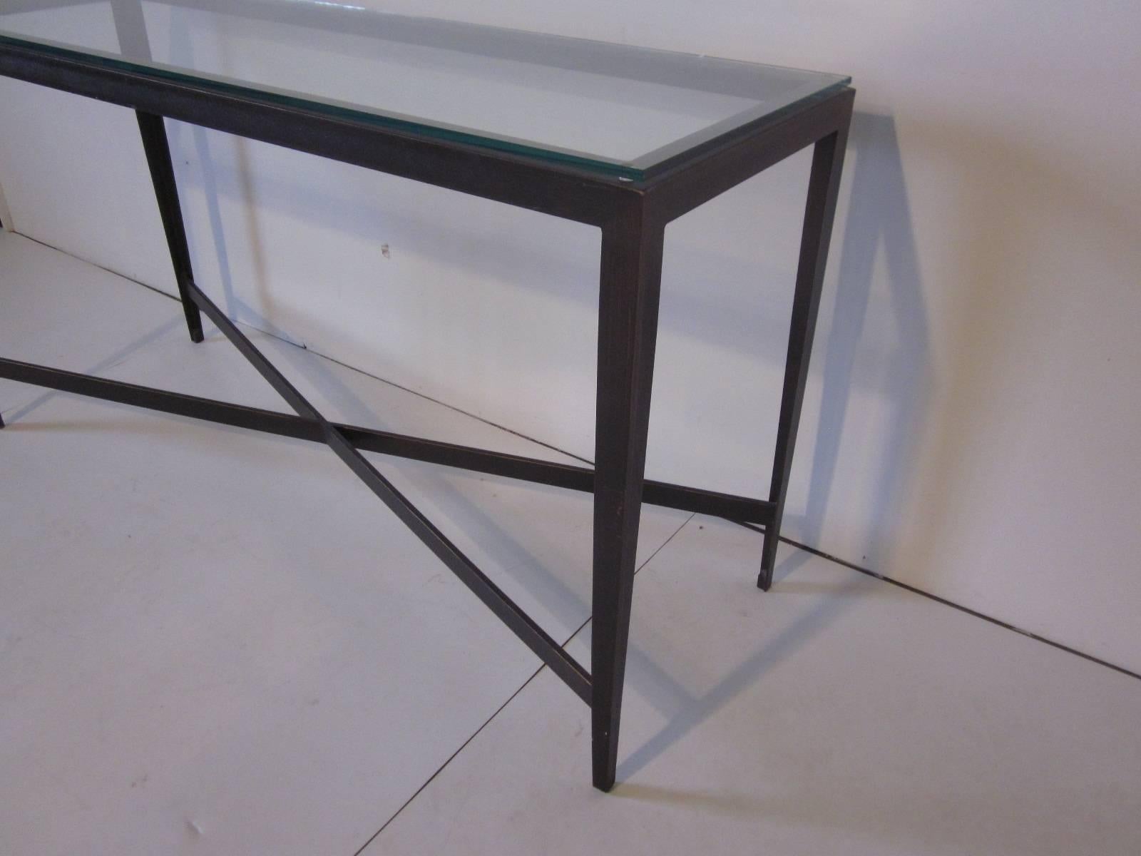 A plate glass topped steel console table in a faux bronze patina finish with crossed stretcher in an upscale Industrial Design look.