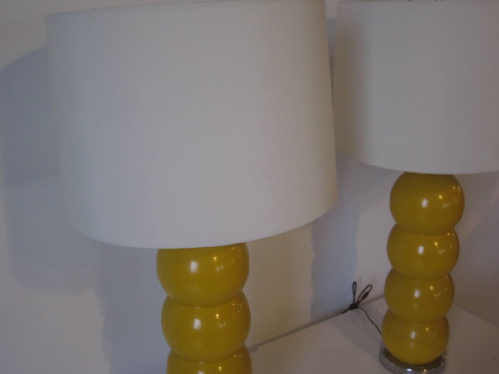 A pair of dark yellow stacking ball table lamps with chrome bases and shafts topped with bone white linen shades, manufactured by the George Kovacs Lighting Company.