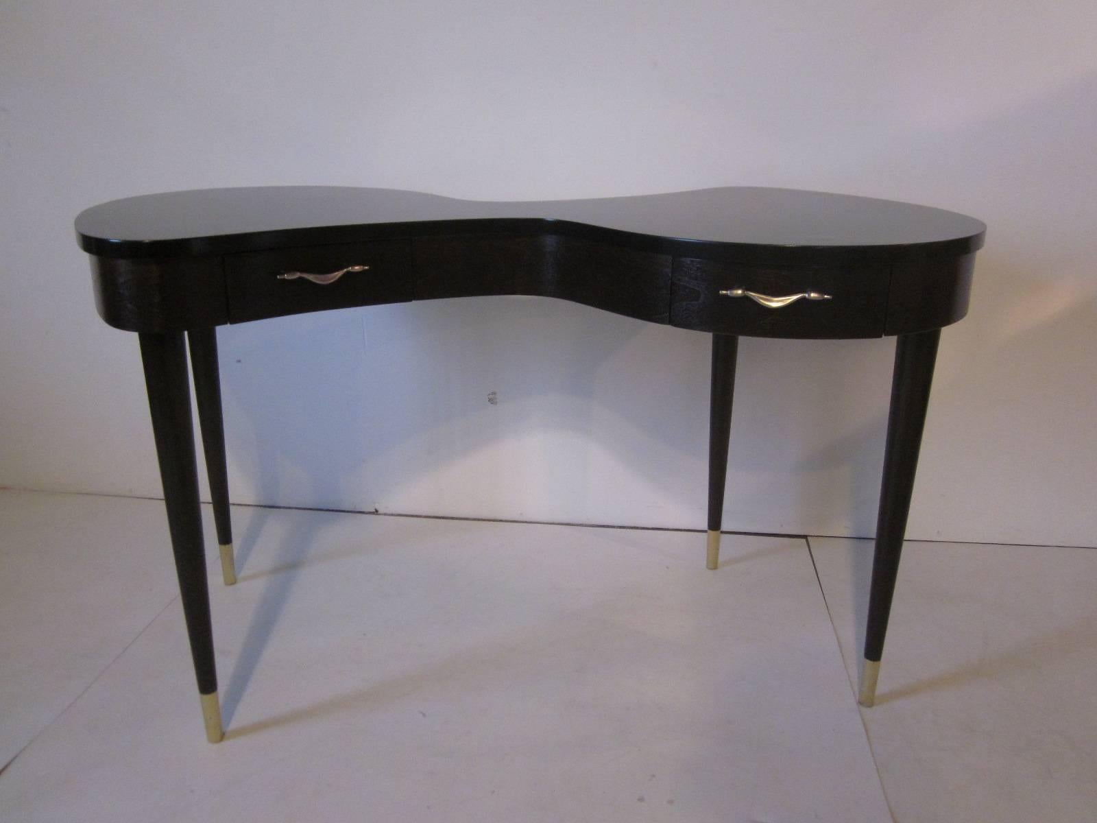 A ebony toned wood vanity with satin black hourglass shaped top, two drawers that have swag styled pewter pulls and long conical legs with brass end caps. In the form of a Italian marker.