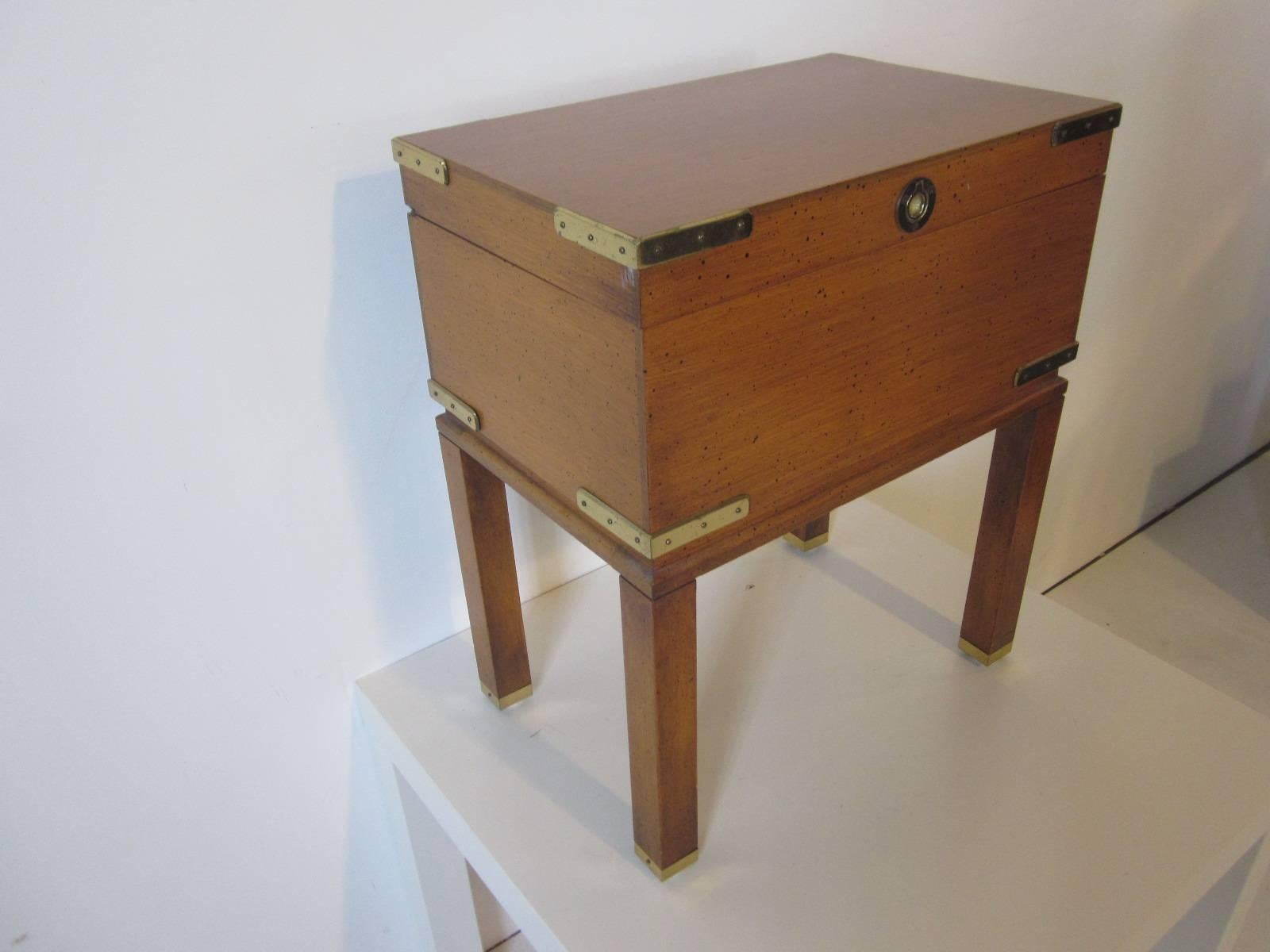 A wooden jewelry chest with brass details, inset ring pull and leg caps finished in a speckled satin black and medium saddle wood tone. Piano hinged flip top lid with spring and finished internal storage area.