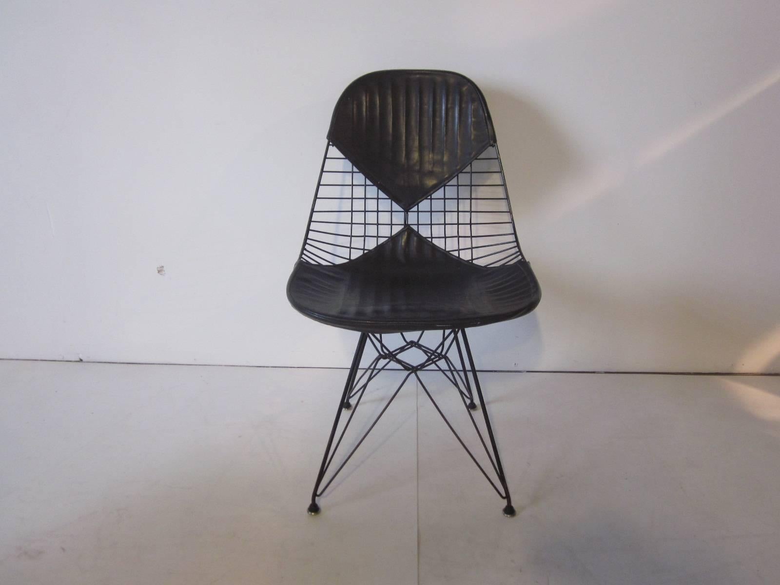 A pair of black metal wire Eiffel tower based chairs with bikini styled Naugahyde seat covers very early production chairs with the self leveling domed floor guides. Manufactured by the Herman Miller Furniture Company.