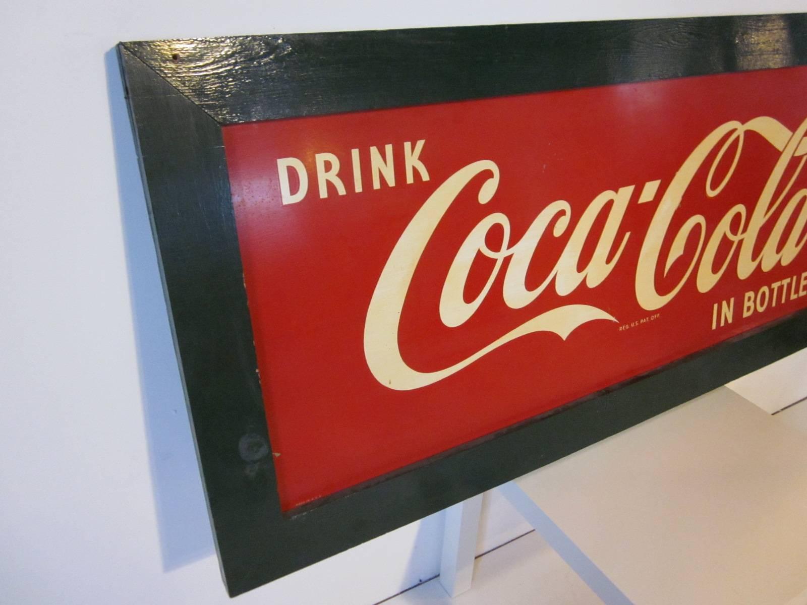 A green wood framed vintage Coca Cola tin sign advertising the beverage in bottles in white and red with small lettering 