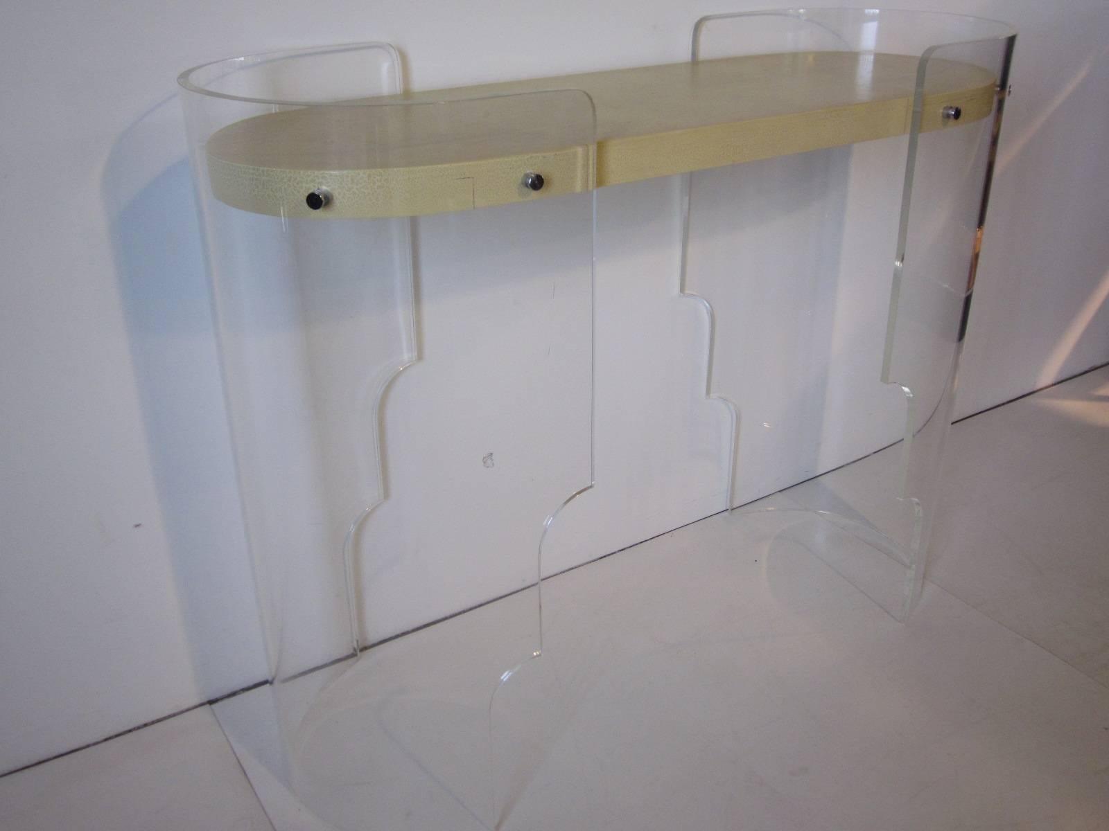 A Lucite console table or bar with curved end pieces and cut a way legs topped by a wood top in an alligator textured painted finish in the manner of Kagan. The wood top to floor measurement is 36