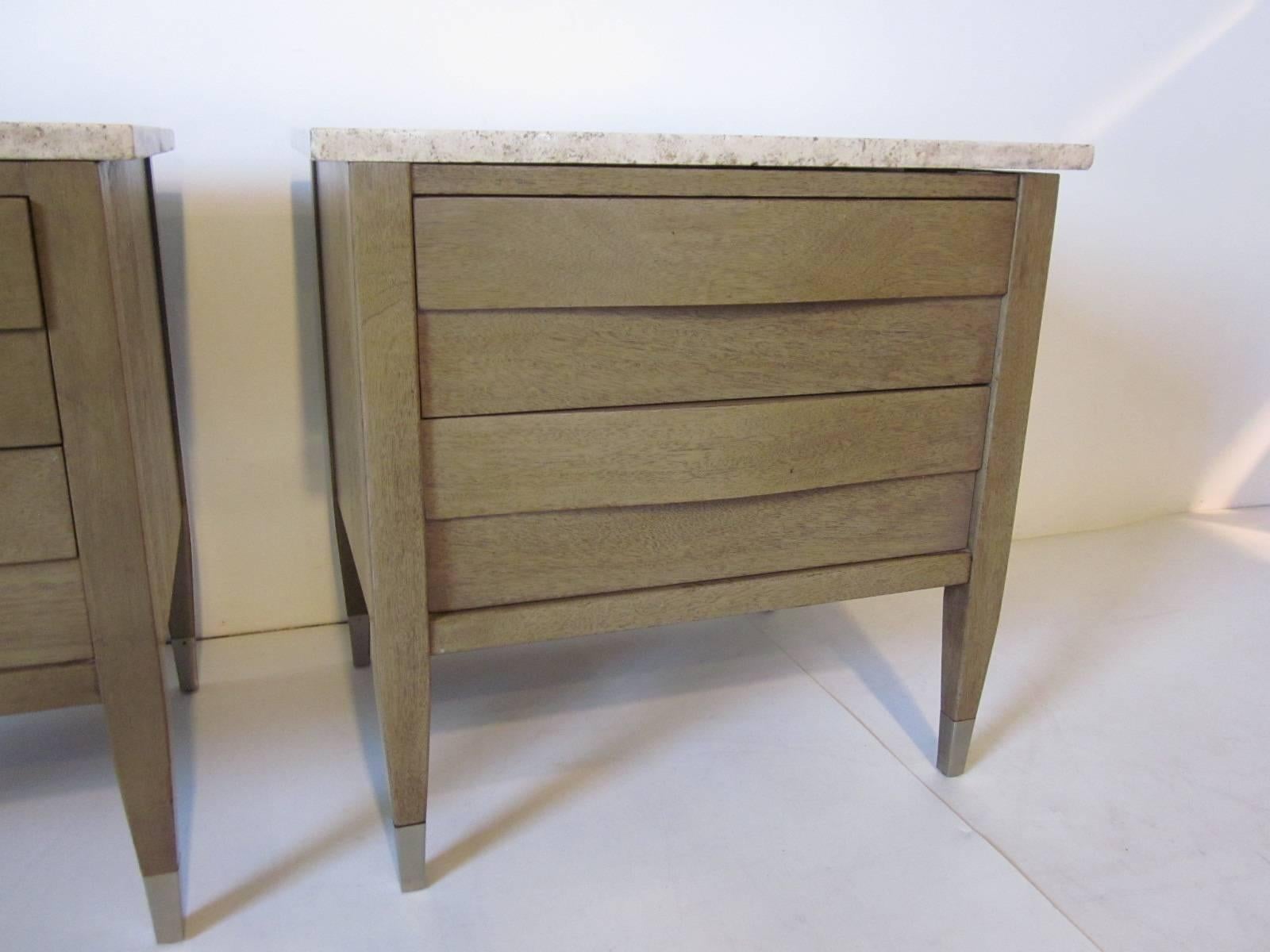 A pair of mahogany nightstands topped with beautiful Italian travertine marble with two sculptural drawer fronts and stainless capped feet. Designed in the style of Singer and Sons but manufactured by American of Martinsville.