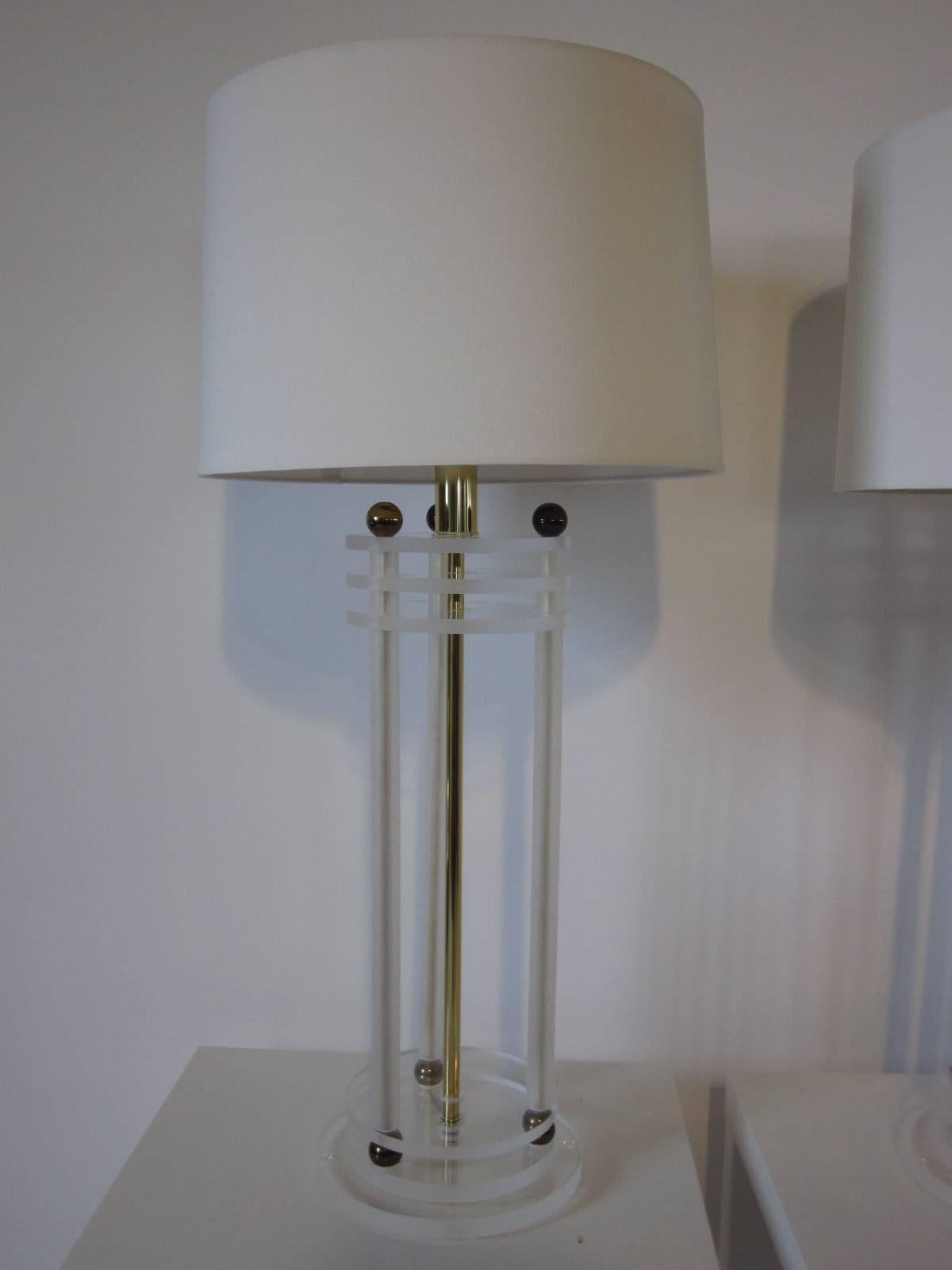 Columned Lucite table lamps with a mix of frosted and clear Lucite complemented with brass balls, rods and original finial topped by an off-white linen shade. Designed in the manner of Frederick cooper shade diameter is 17