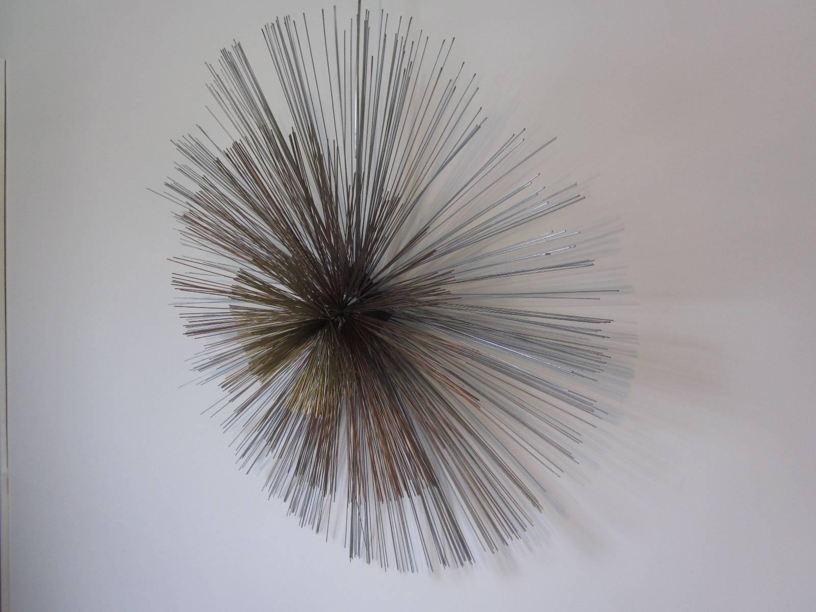 A starburst wall sculpture using three different types of heavy duty metal wire, brass center, copper inner ring and a stainless steel outer ring all in which can be spun around. A wonderful textured piece of art with a steel mounting plate attached