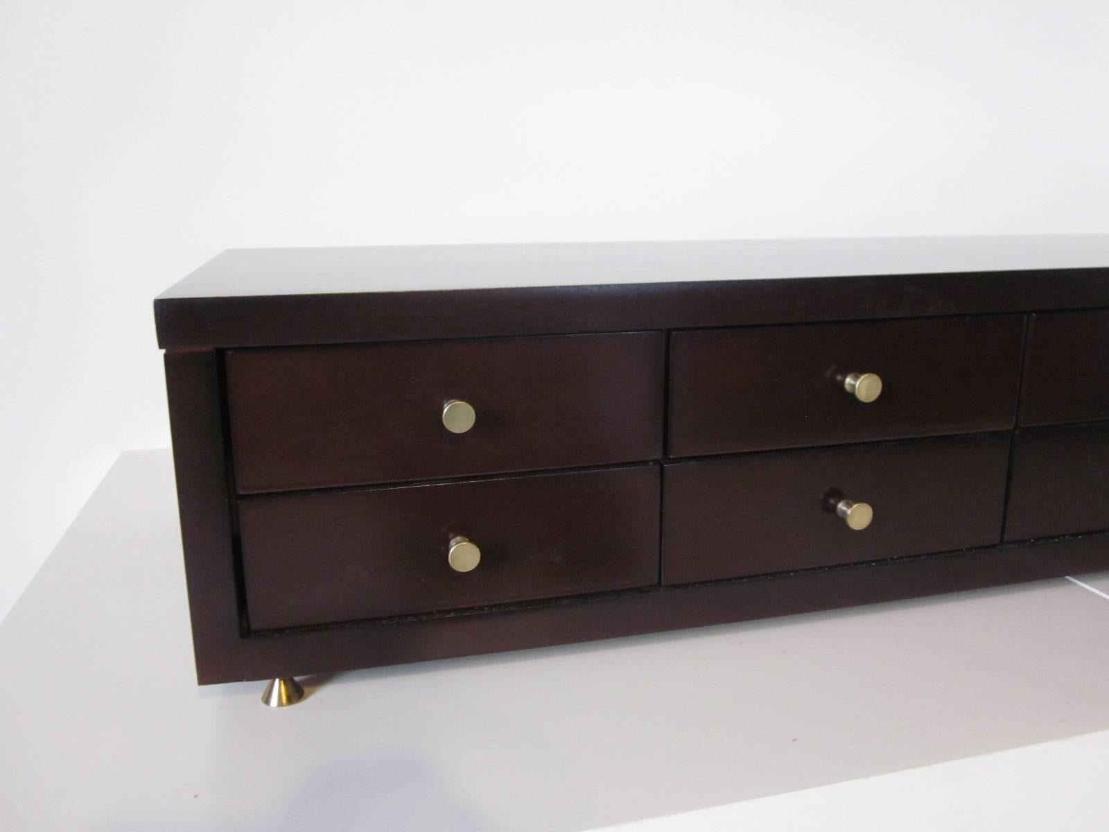 A ten-drawer McCobb jewelry chest in a dark ebony finish with brass pulls and small brass feet. Retains the manufactures label to the inside drawer, by the Winchendon Furniture Company.