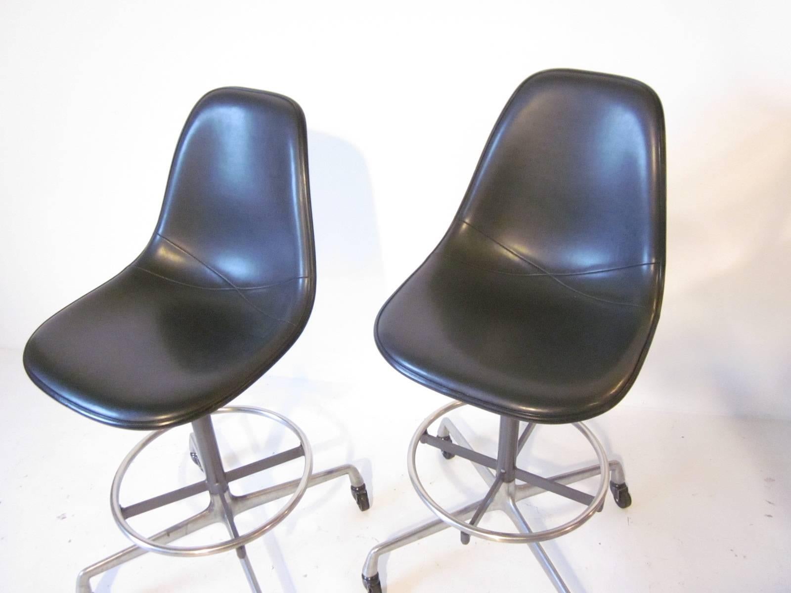 Upholstered Eames architectural rolling stools with adjustable seat height and chrome foot rest. Manufactured by the Herman Miller Furniture Company, seat height is 27