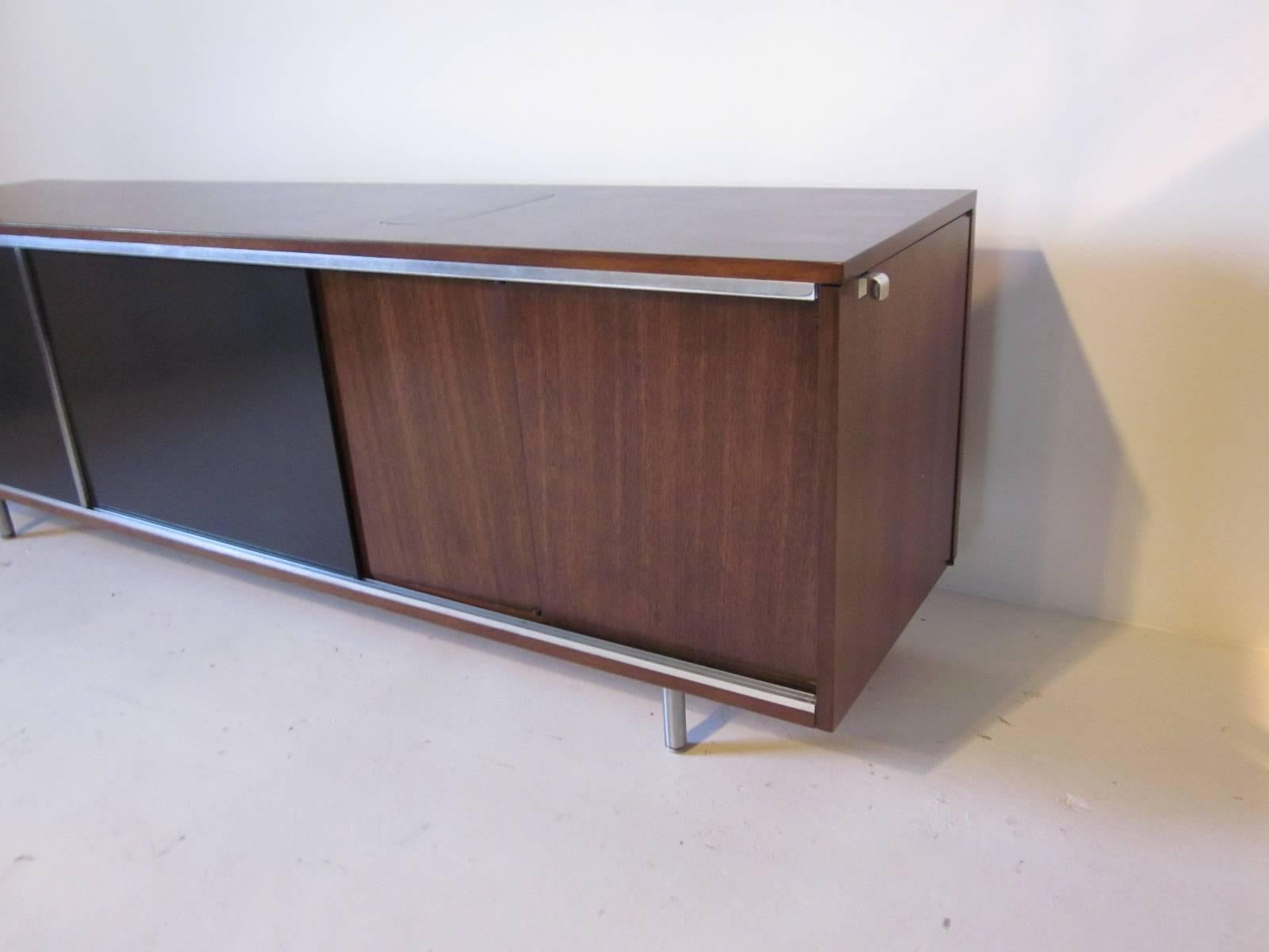 A Nelson walnut credenza with double dark gray black sliding doors, banks of small and large file styled drawers to the inside. Storage to the other side and to the end of the credenza with a shelve, very small trap door to the top right side of the