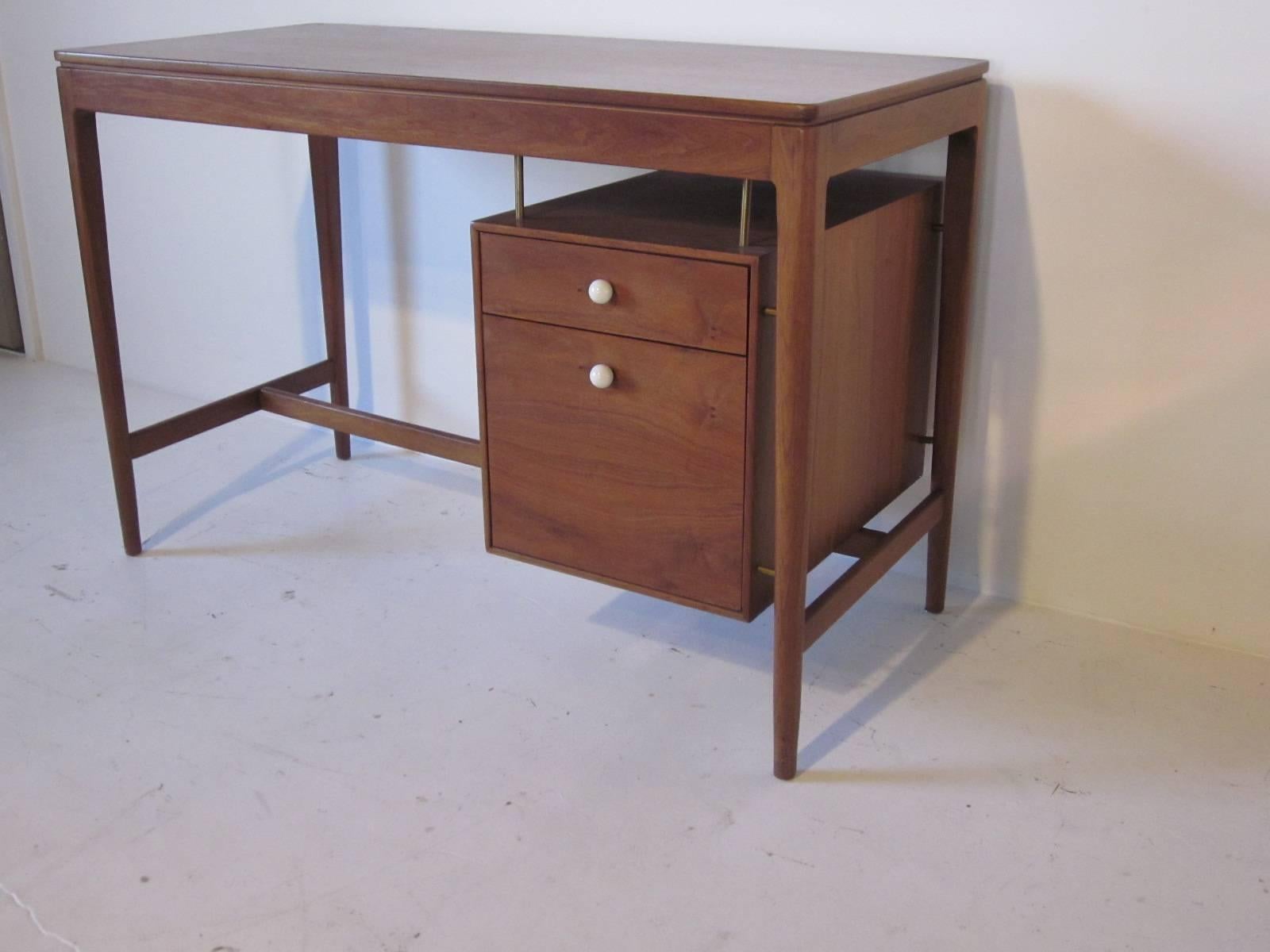 A medium colored walnut desk with hanging drawer and file box , brass details and white porcelain pulls. A great designed desk for a small space or home office, manufactured by the Drexel Furniture Company.