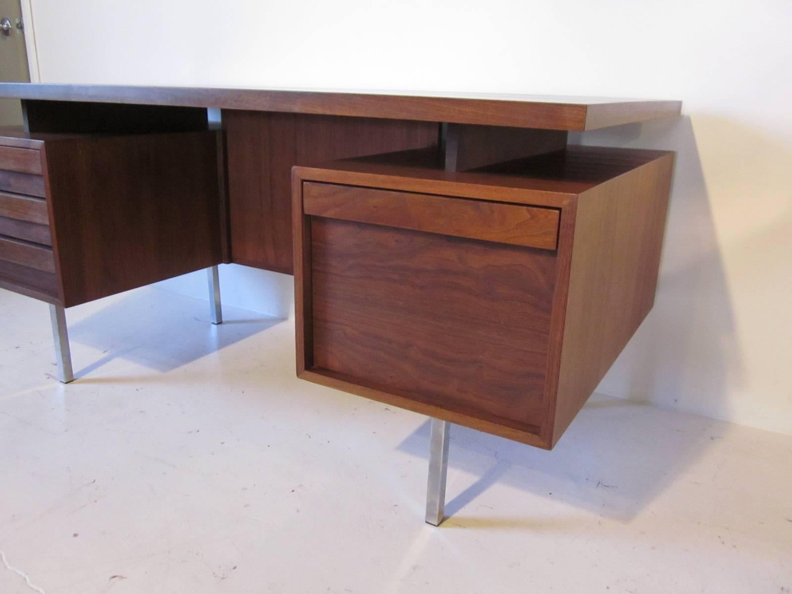 A rich dark walnut floating top desk with two banks of drawers, three to one side and a single file drawer to the other all sitting on square chromed metal legs. A bookcase is built into the other side with plenty of room making this desk great for