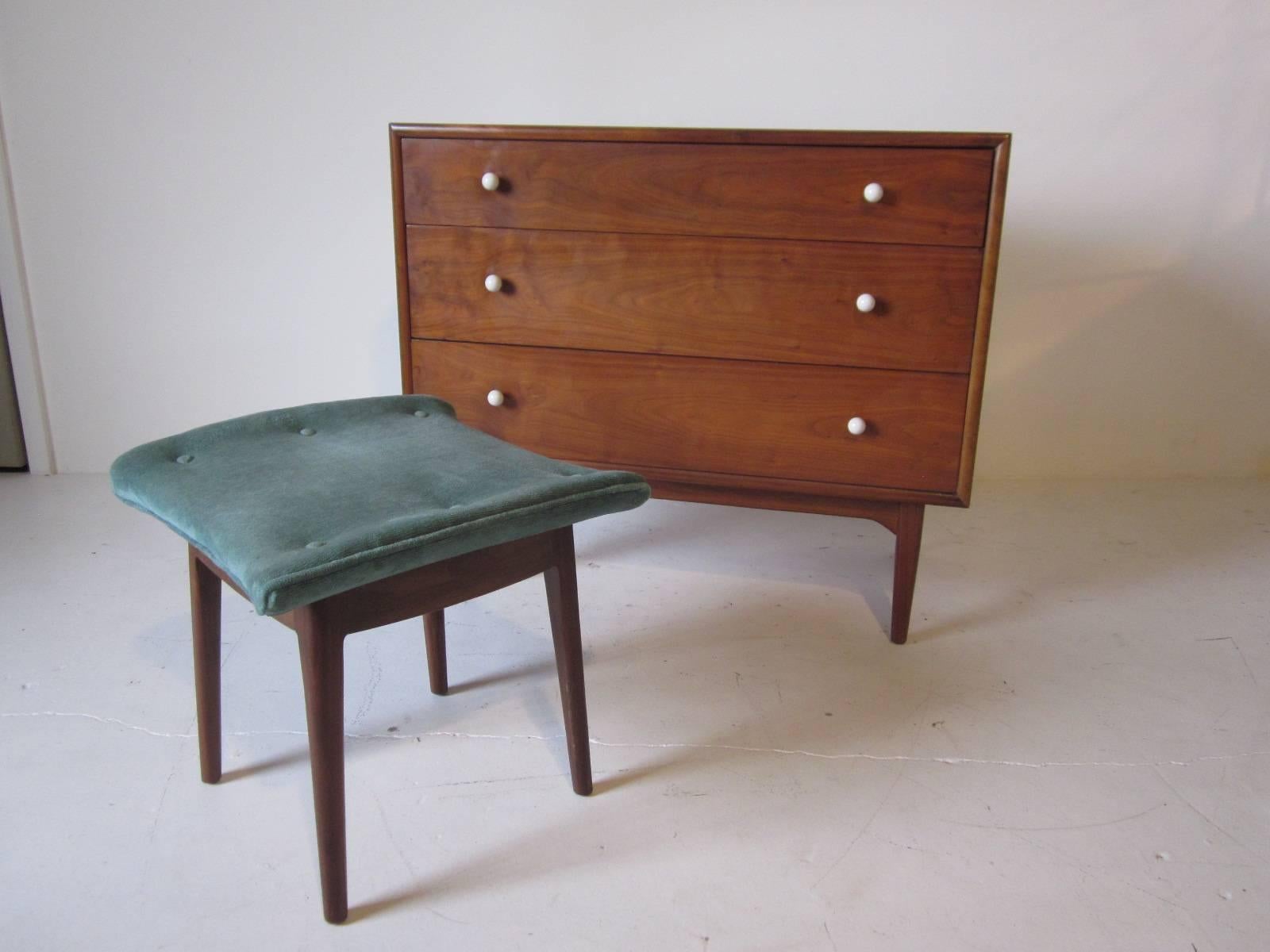 A walnut chest with round white knobs and pull-out hidden vanity, the wood surface flips up reveling a mirror, storage space and sliding white milk glass make-up shelve. Included is the rare matching upholstered stool with walnut legs manufactured