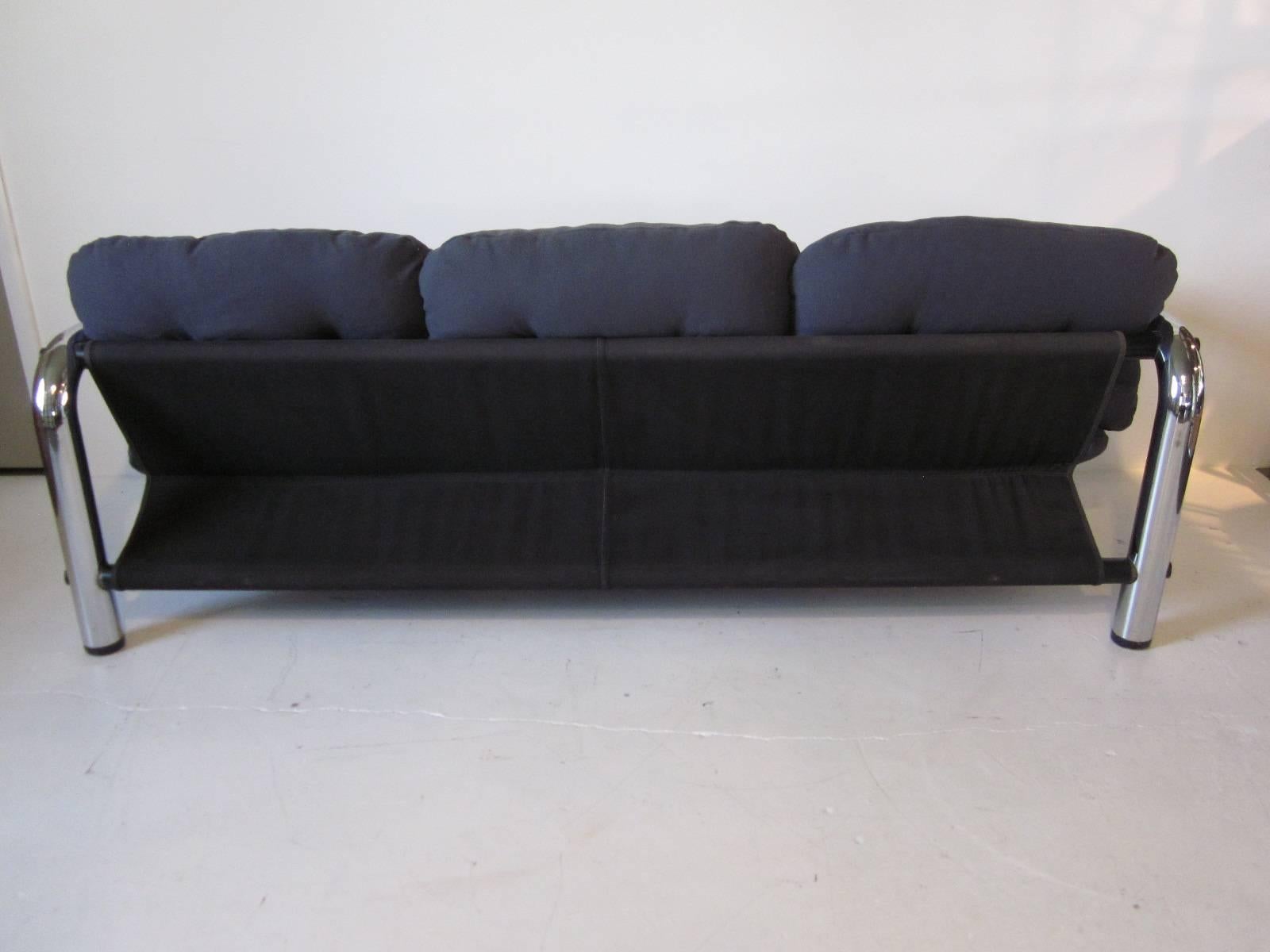 A modern styled tubular chrome metal sofa with charcoal toned canvas sling support topped with comfy gray steel blue upholstered cushions. A true design statement from the swing'in 1970s Op Art movement.