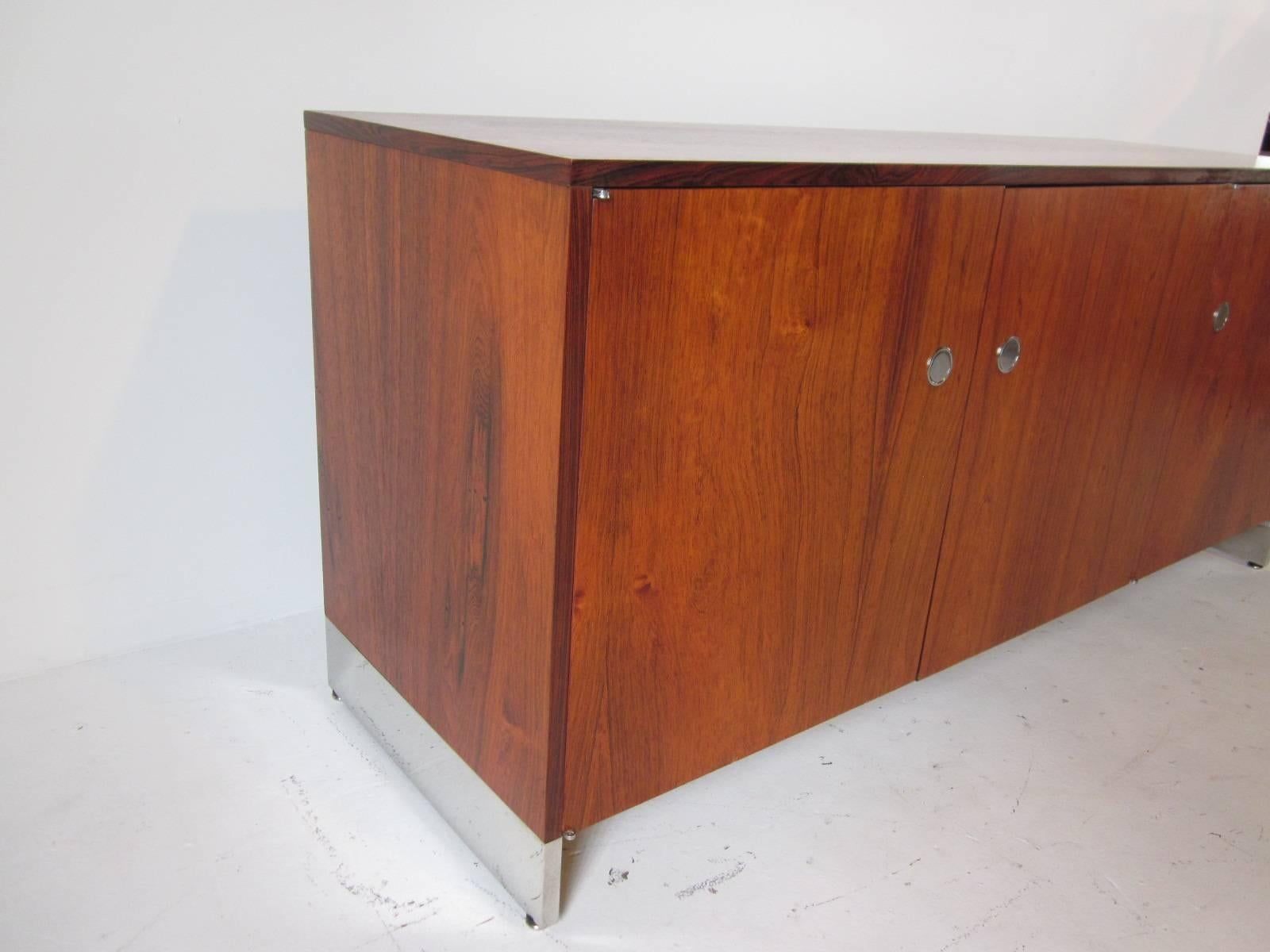 A well grained Brazilian rosewood three-door credenza with chrome disk flip pulls and chrome plinth styled legs. Inside there are two adjustable shelves and the back side of the credenza is covered in the same rosewood so this piece can float or