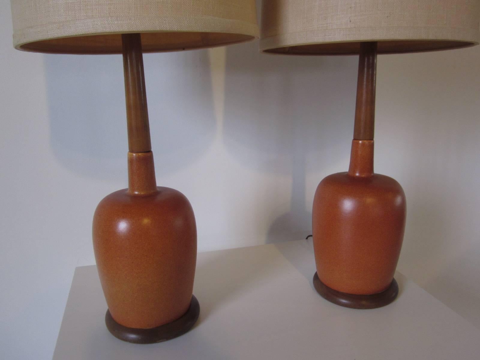 A pair of burnt orange / rust toned pottery table lamps with teak wood base plate and stem topped with the original linen shades, made in Denmark .