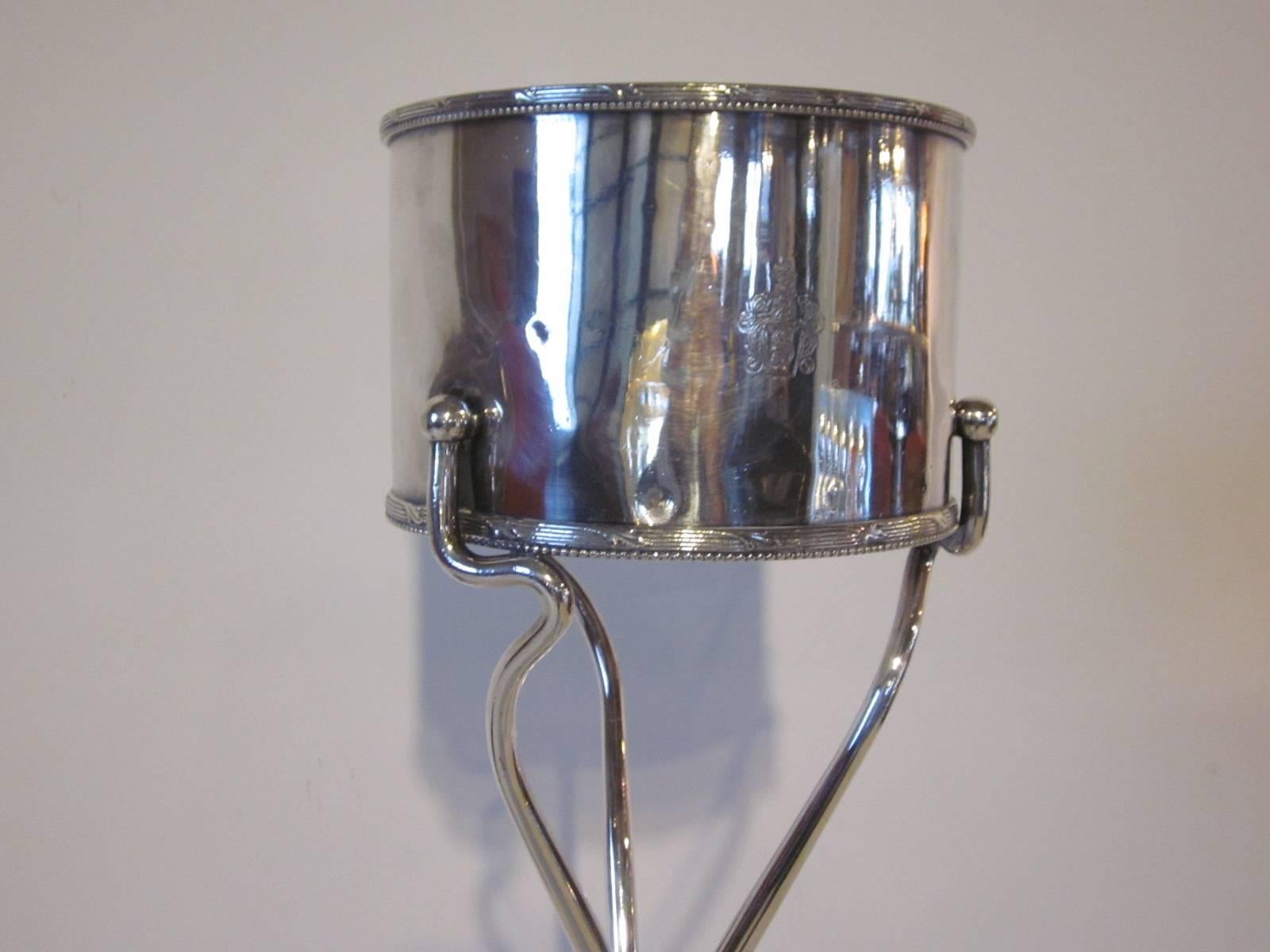 A one piece silver plated hotel ice bucket on a matching Stand in a mix of Mid-Century and classic design. Modern styled base with ball feet and simple bucket with some laurel designs to the top and bottom edge. Manufactures markings to the bucket