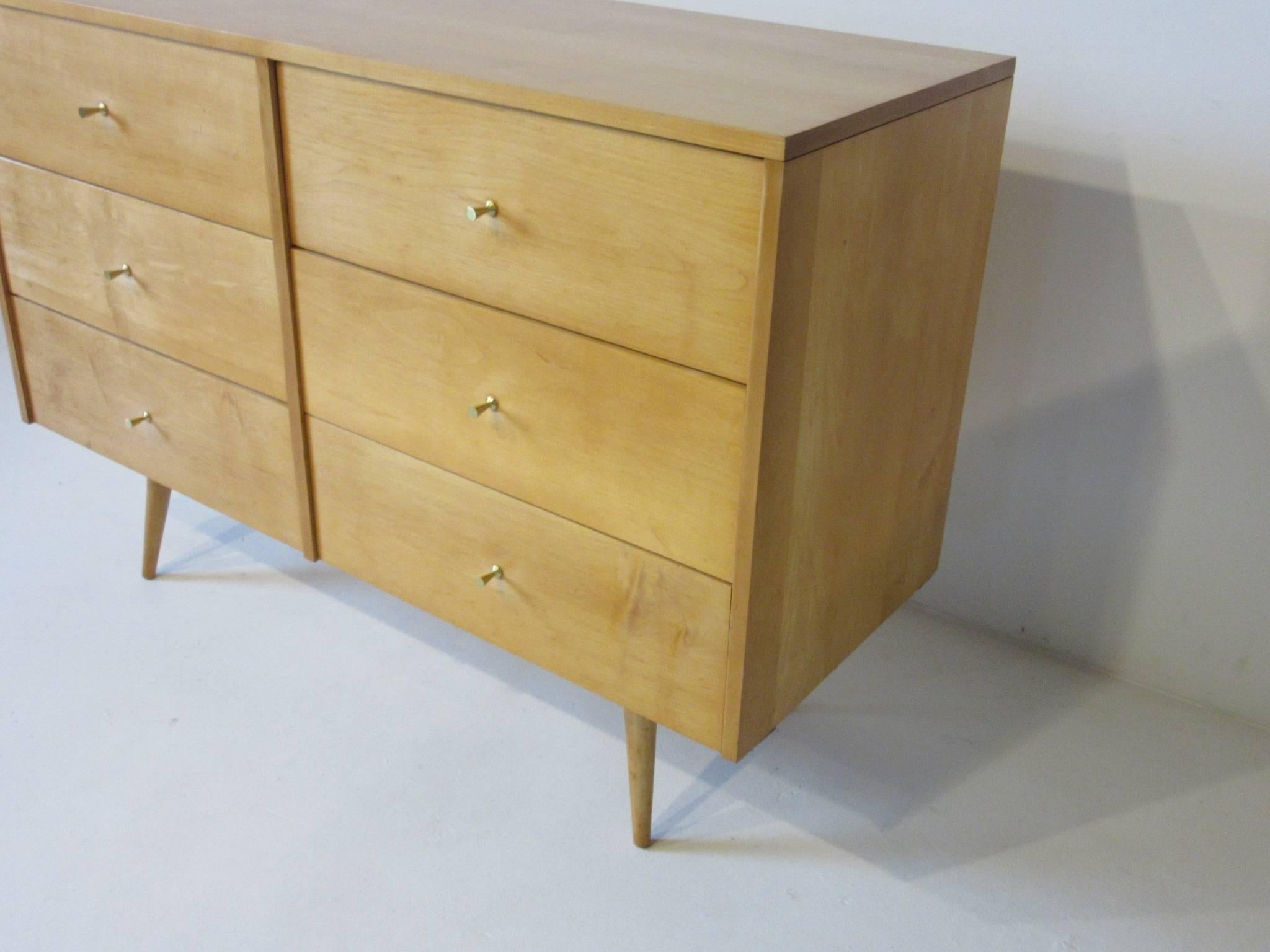 A McCobb solid maple six-drawer dresser chest in a honey toned finish with brass Tee pulls sitting on matching conical legs. From the Planner Group Line and manufactured by the Winchendon Furniture Company.