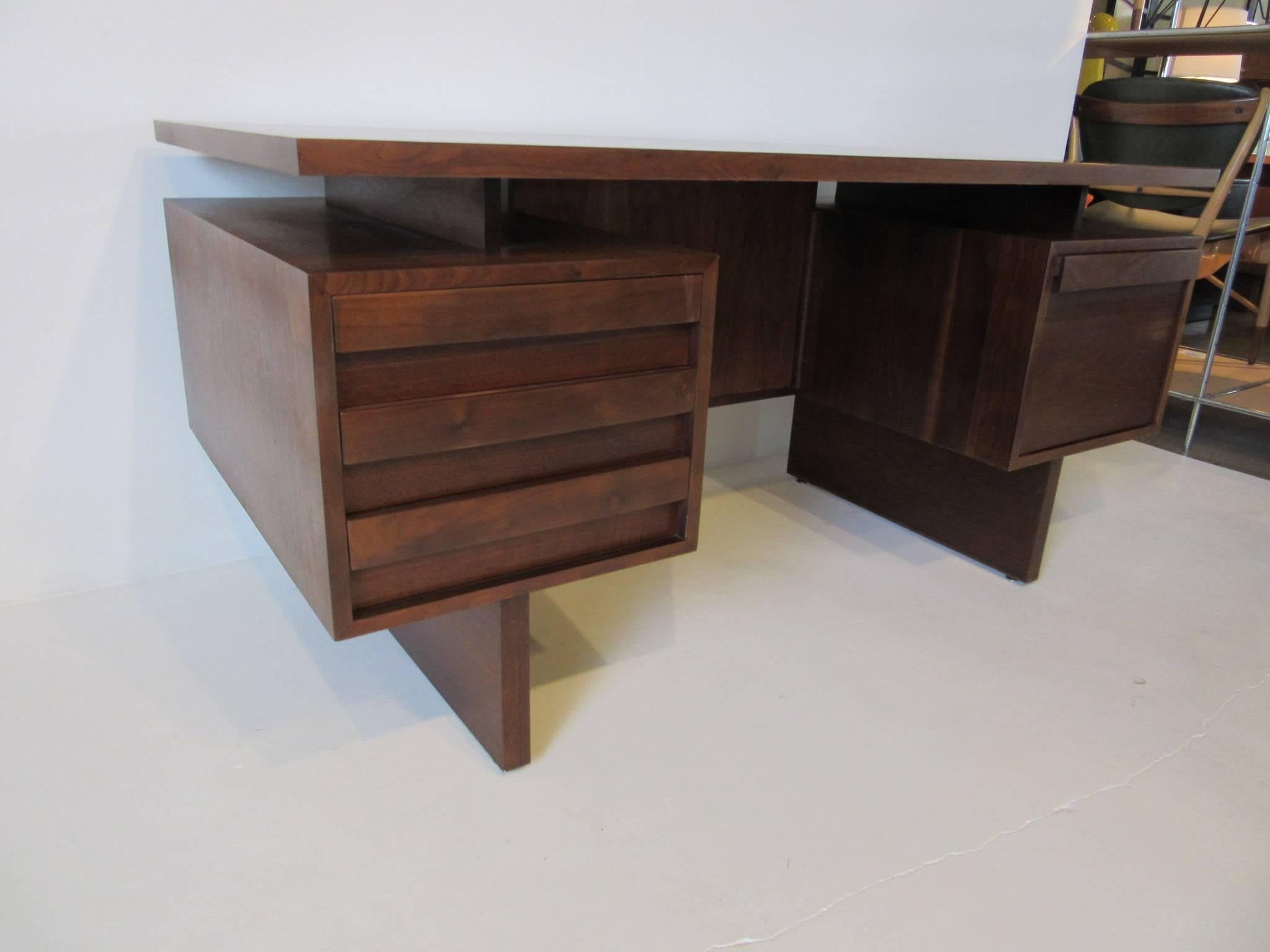 A dark walnut floating top executive desk with three drawers to the left for storage and a large file drawer to the right. Built into the backside of the desk are three book shelves with plinth styled legs .