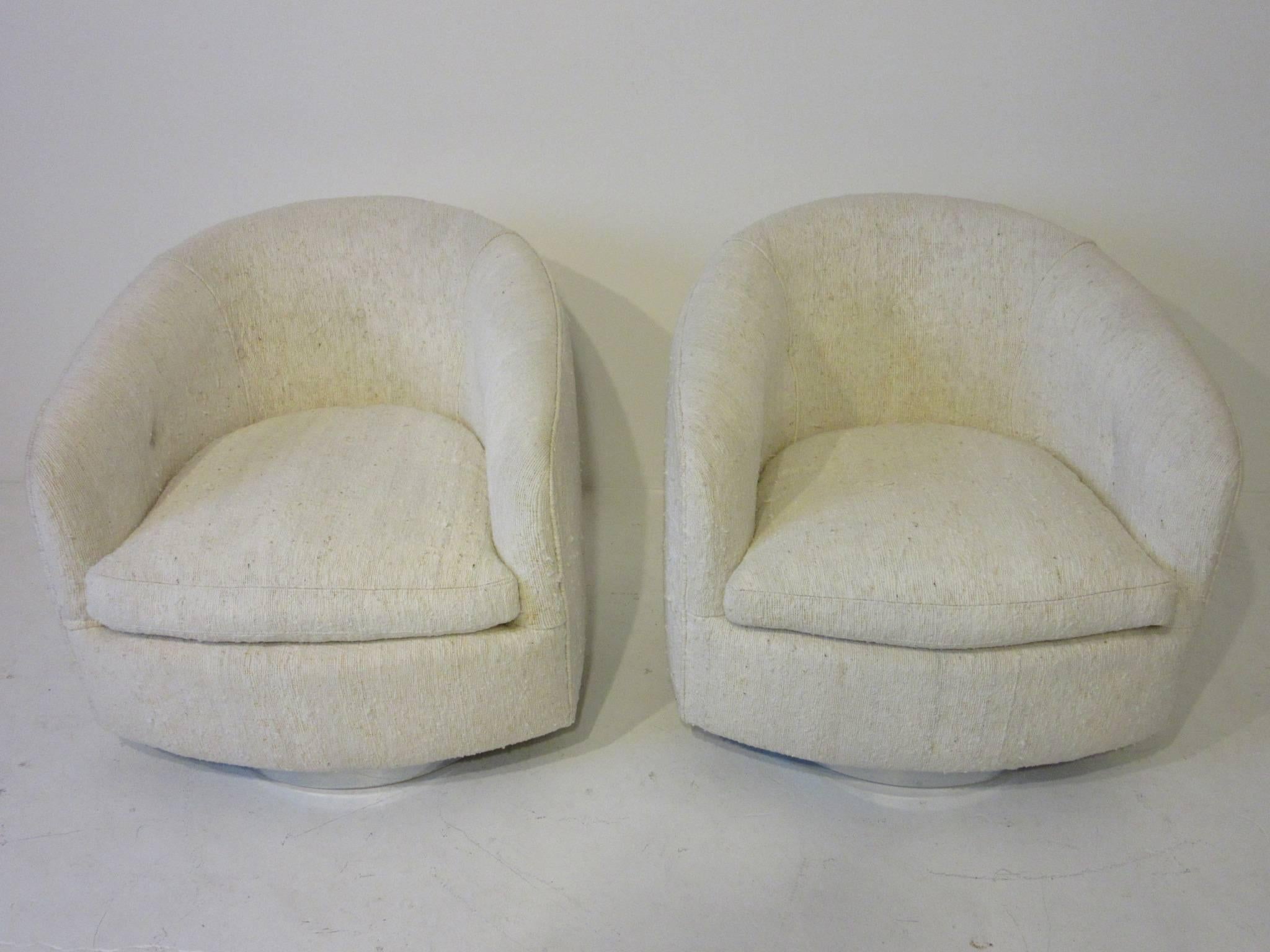 A pair of Milo Baughman swivelling and rocking barrel back club chairs with chrome bases upholstered in a natural nubby woven cotton silk blended fabric, retains the manufactures label Thayer Coggin by Milo Baughman.