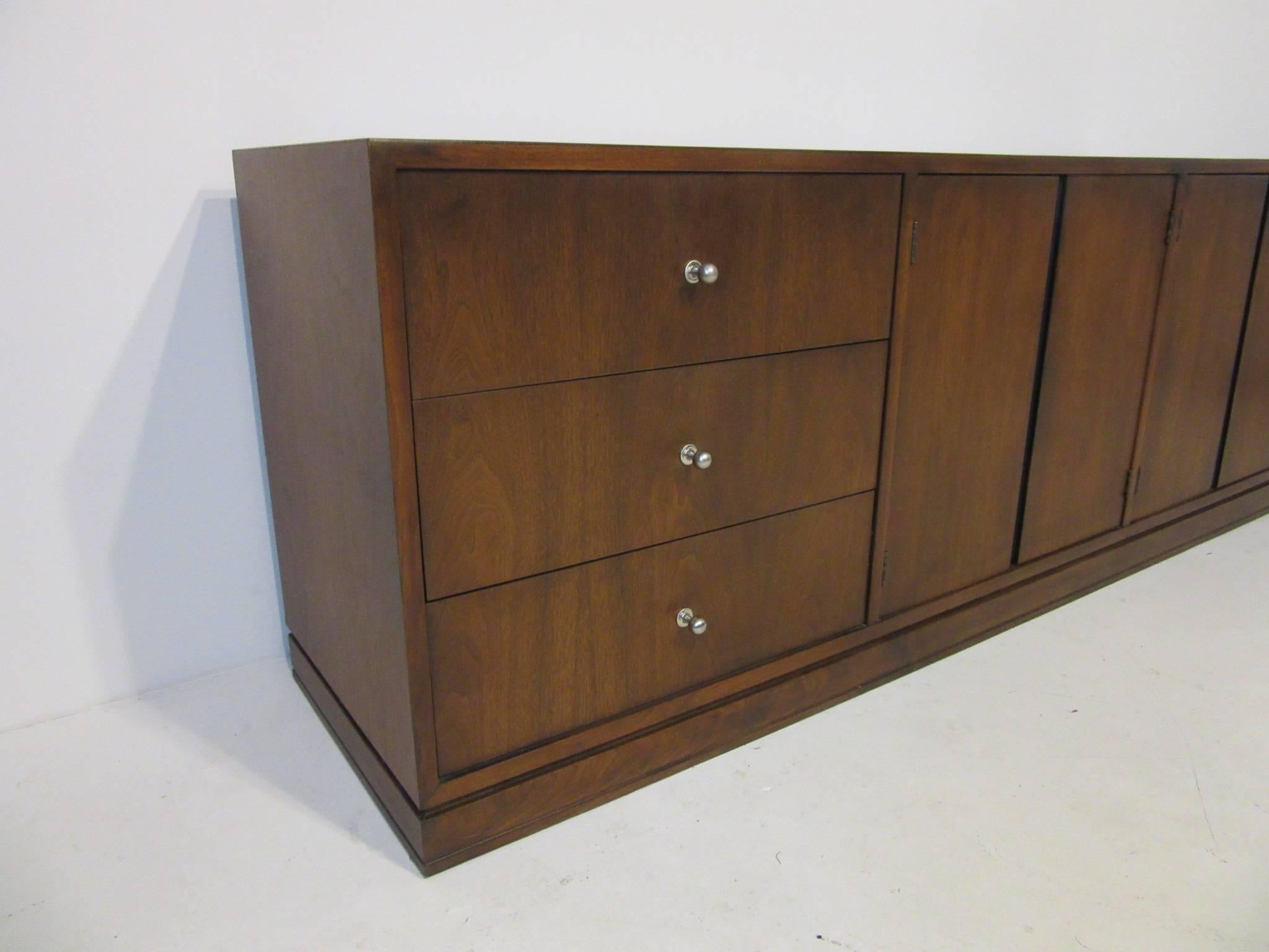 A Mid-Century walnut credenza or sever having three drawers detailed with brushed stainless pulls and four doors each with an adjustable shelve. Designed in the manner of Harvey Probber.